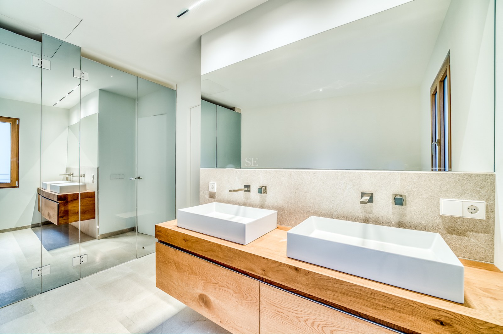 Salle de bains moderne avec meuble suspendu en chêne, double vasque blanche et grand miroir sans cadre.