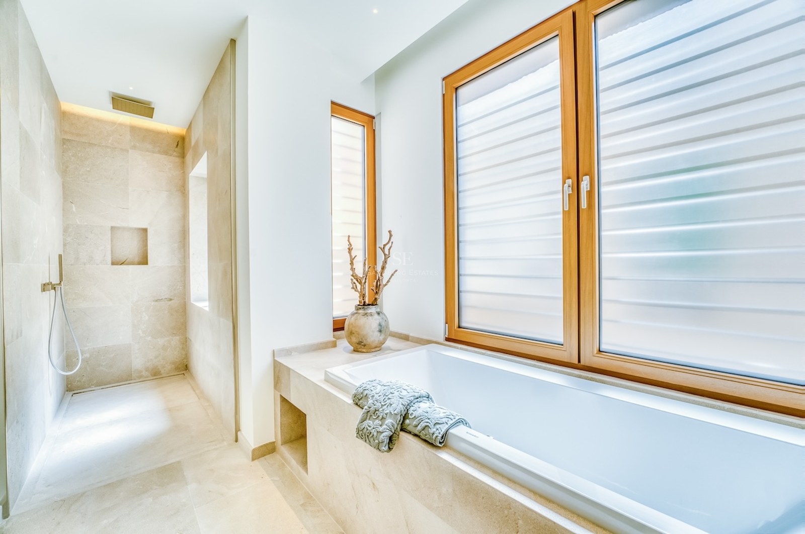 Modern bathroom featuring a built-in bathtub, walk-in rain shower, and natural stone tiling with oak window frames.