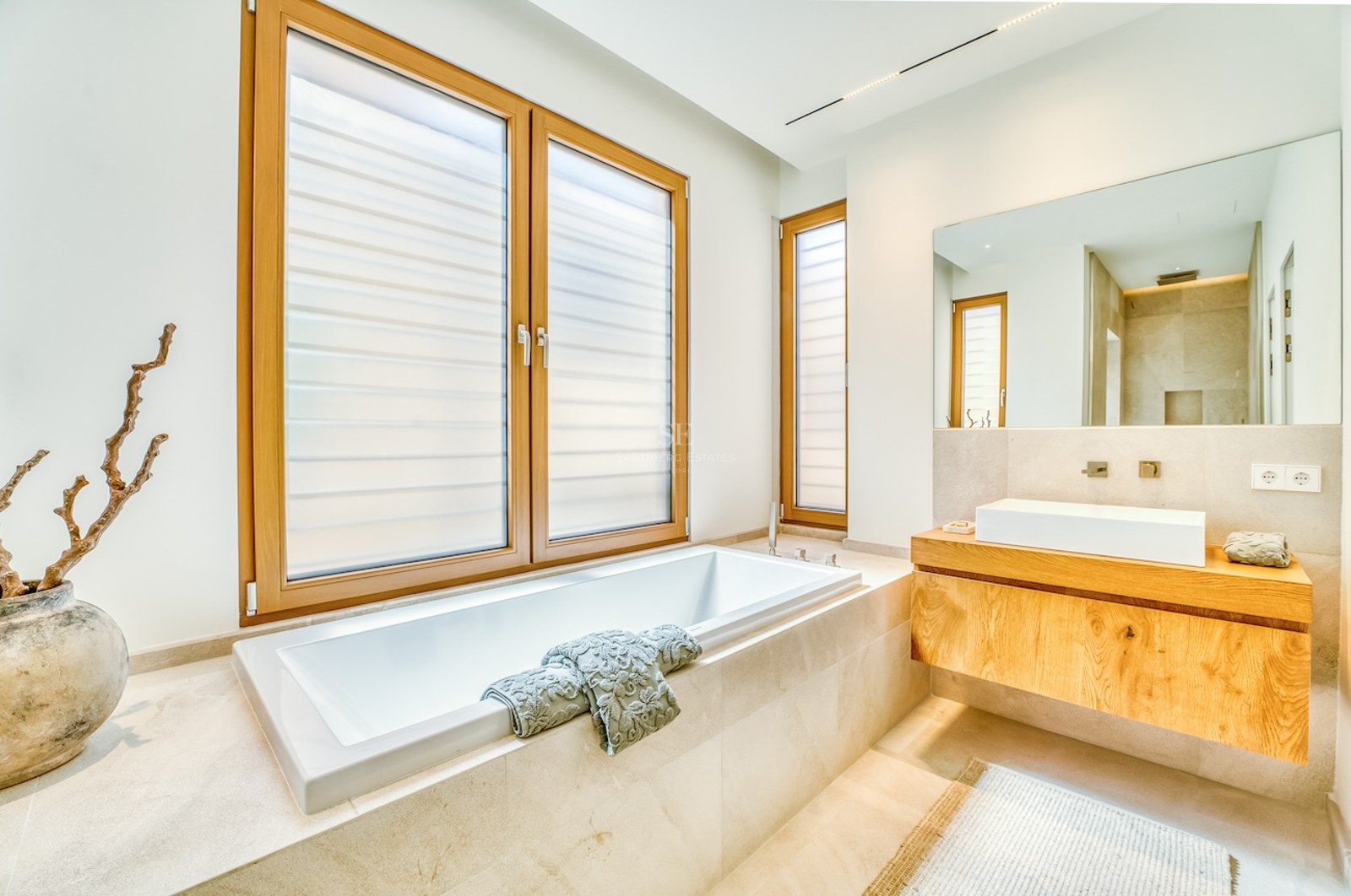 Minimalist bathroom featuring a built-in white bathtub, oak floating vanity, and natural stone tiling.