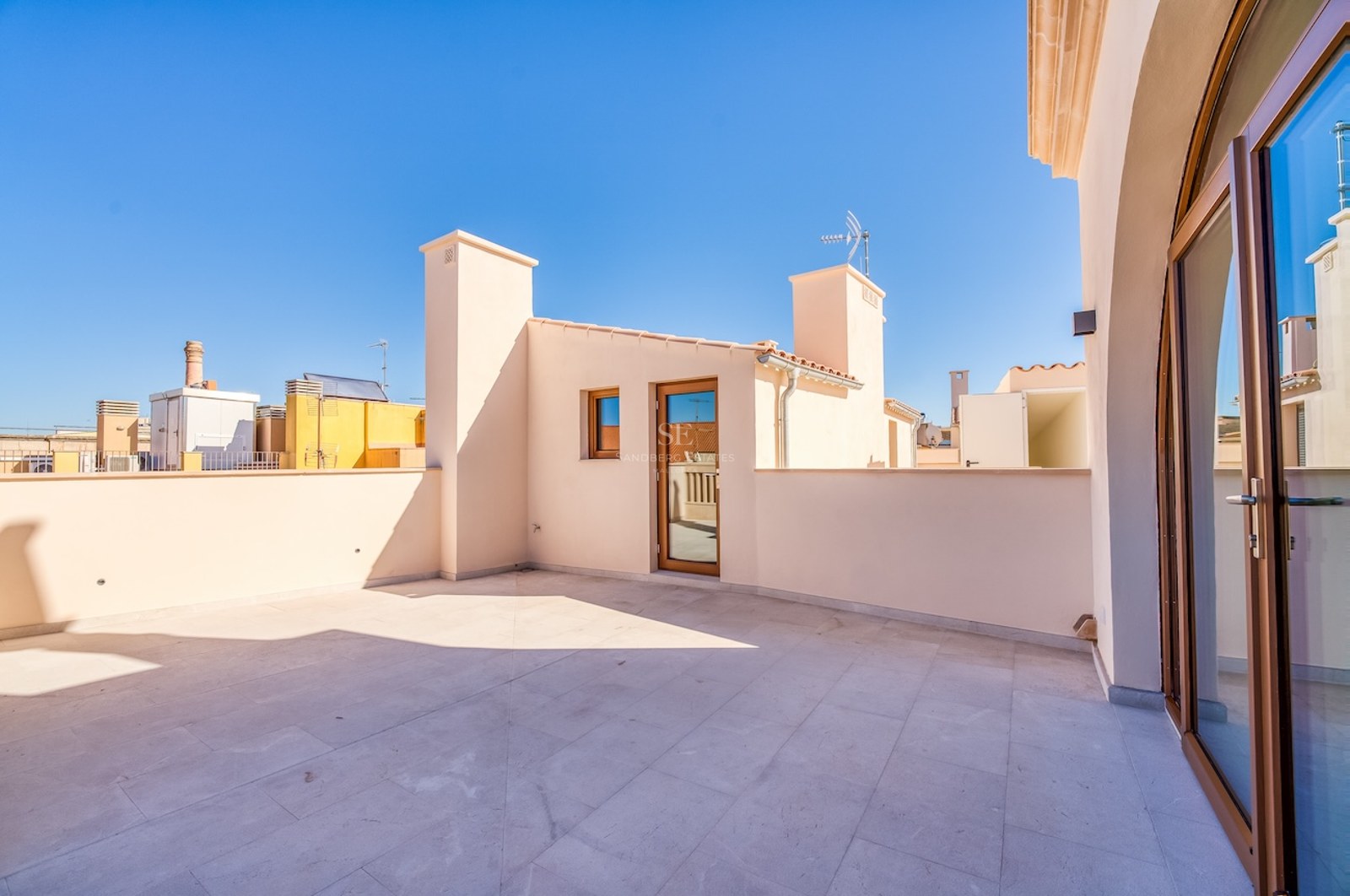 Large rooftop terrace with natural stone tiling and cream walls under a clear blue sky.