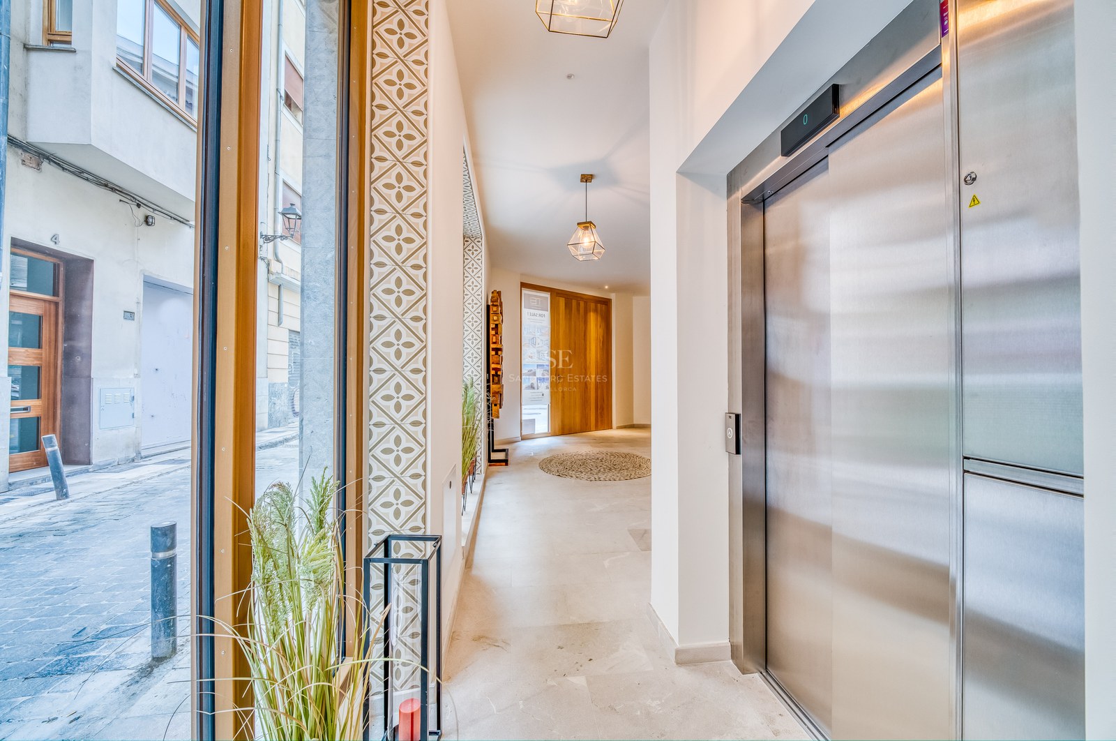 Entrée lumineuse avec baies vitrées, ascenseur en acier inoxydable et carrelage mural décoratif.