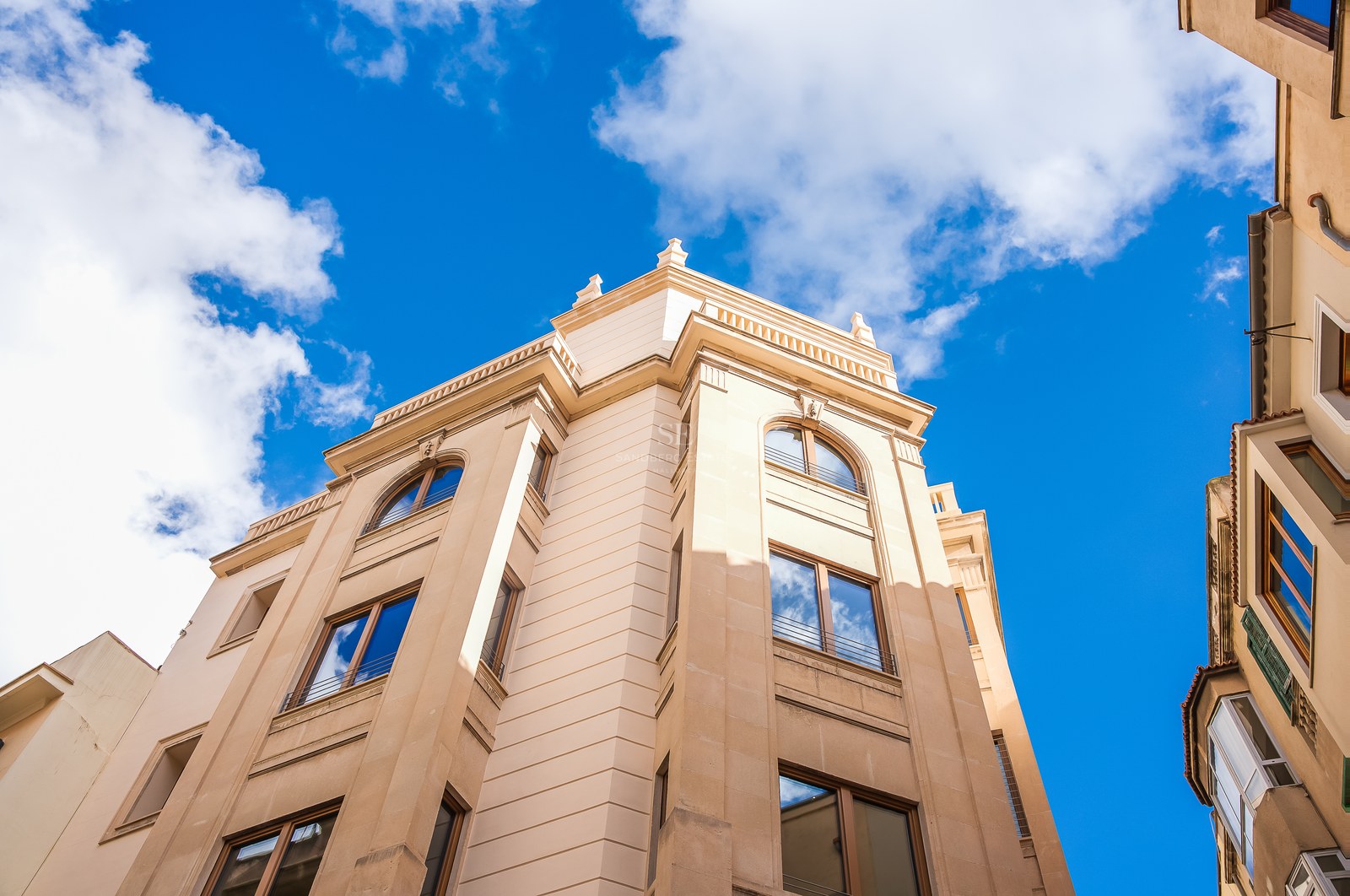 Low-angle view of a beige natural stone building facade with wooden window frames against a clear blue sky.