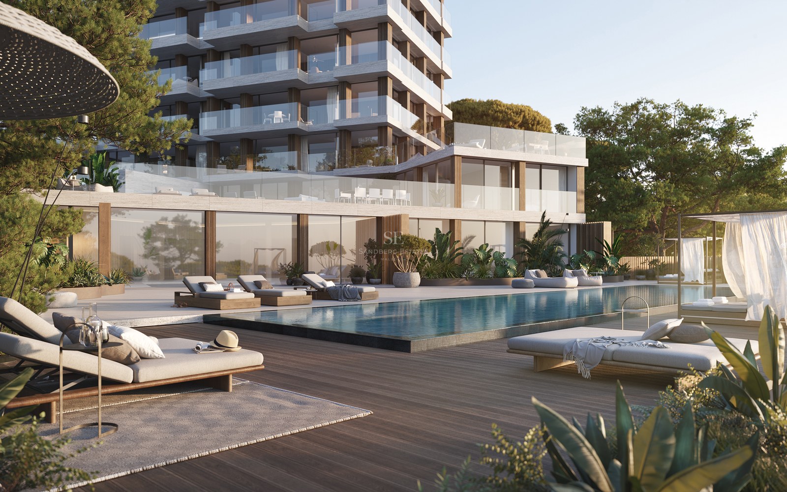 Modern apartment building with a large swimming pool, wooden deck, luxury lounge chairs, and lush green gardens.