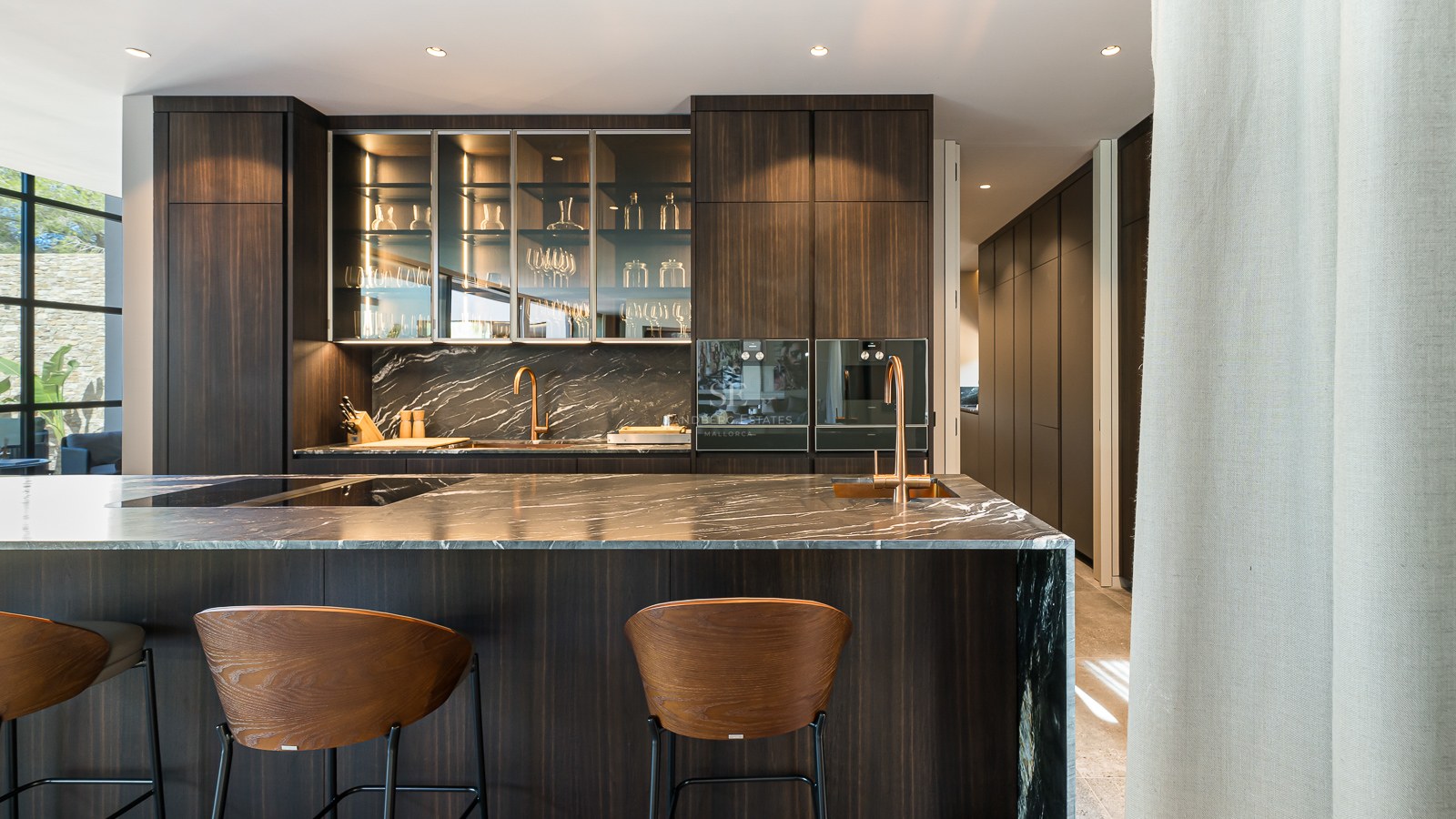 Contemporary kitchen featuring a dark veined marble island, wooden bar stools, and elegant copper fixtures.