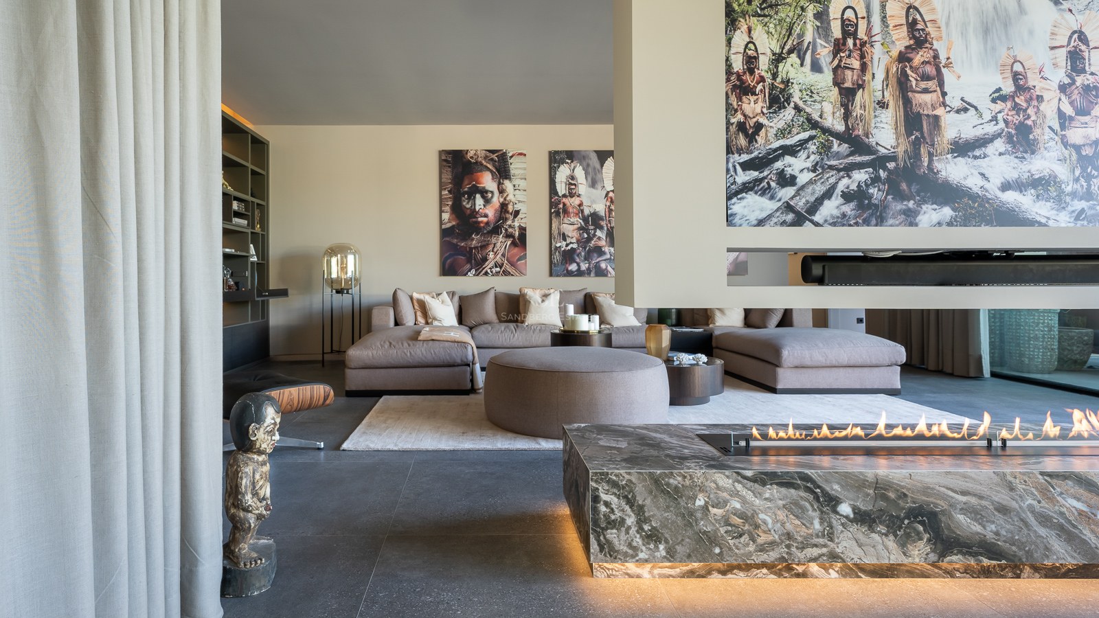 Luxury living room featuring a grey sectional sofa, a linear marble fireplace, and tribal artwork on the walls.