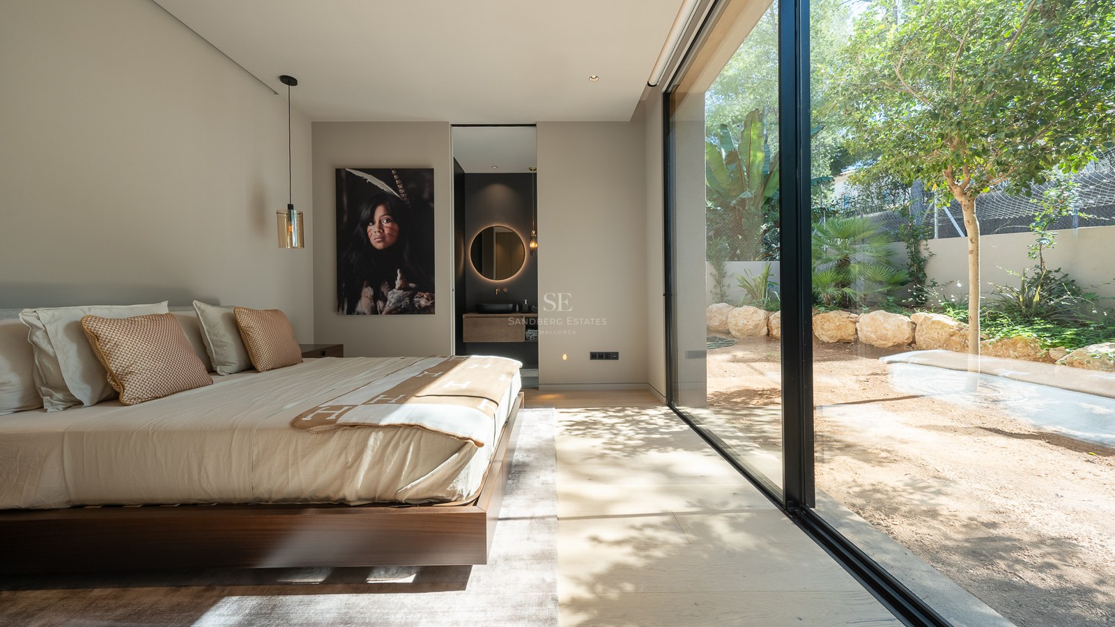 Modern bedroom featuring floor-to-ceiling glass doors to a garden, walnut wood bed frame, and ensuite bathroom.