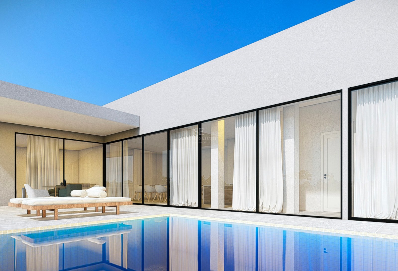 Modern white villa with floor-to-ceiling glass windows overlooking a blue swimming pool and stone terrace with sun loungers.
