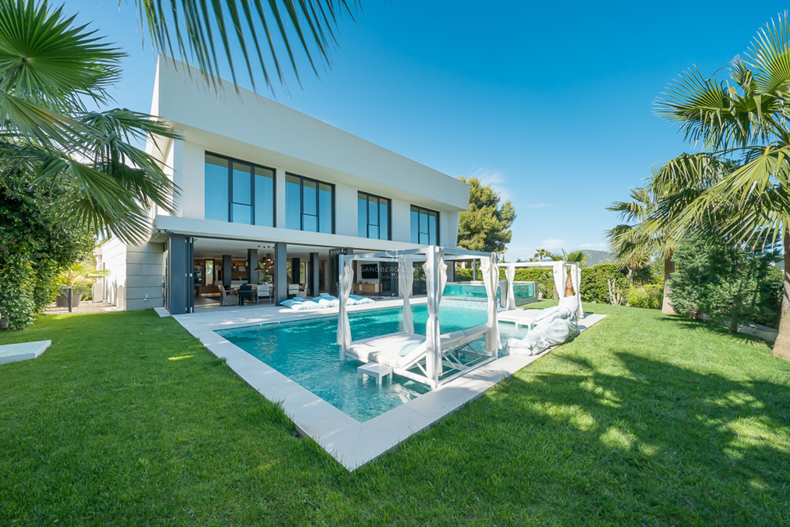 Vue de la piscine turquoise entourée d'une végétation luxuriante et d'une architecture moderne. Chaises longues et parasols blancs invitent à la détente.