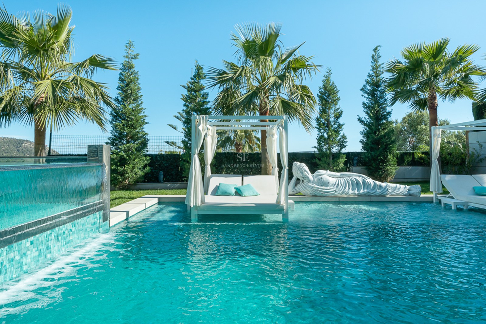 Vue sur piscine à débordement avec chaises longues, entourée d'un jardin luxuriant. Architecture moderne avec larges fenêtres et balcon.