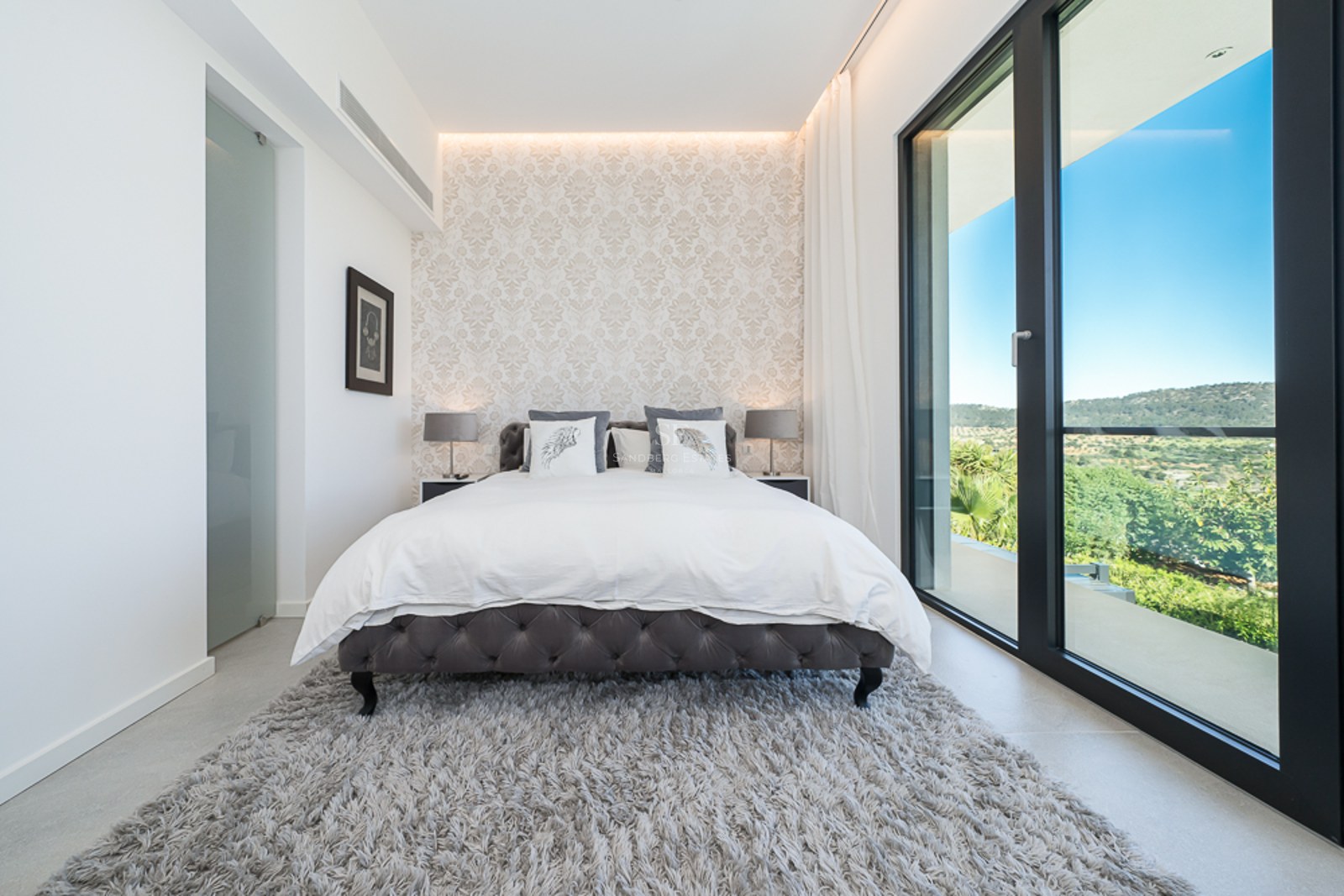 Vaste salon avec de grandes baies vitrées, parquet clair, lumière naturelle et décoration minimaliste. Vue sur un jardin luxuriant.