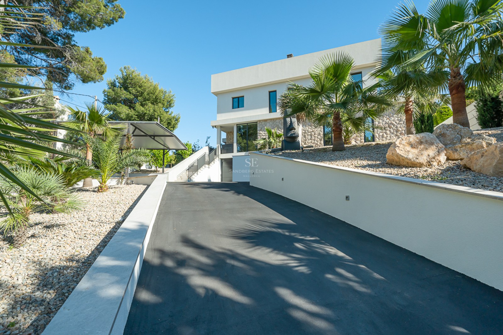 Grande piscine avec transats, jardin verdoyant et façade moderne d'une maison individuelle avec de grandes fenêtres. Ciel bleu dégagé.