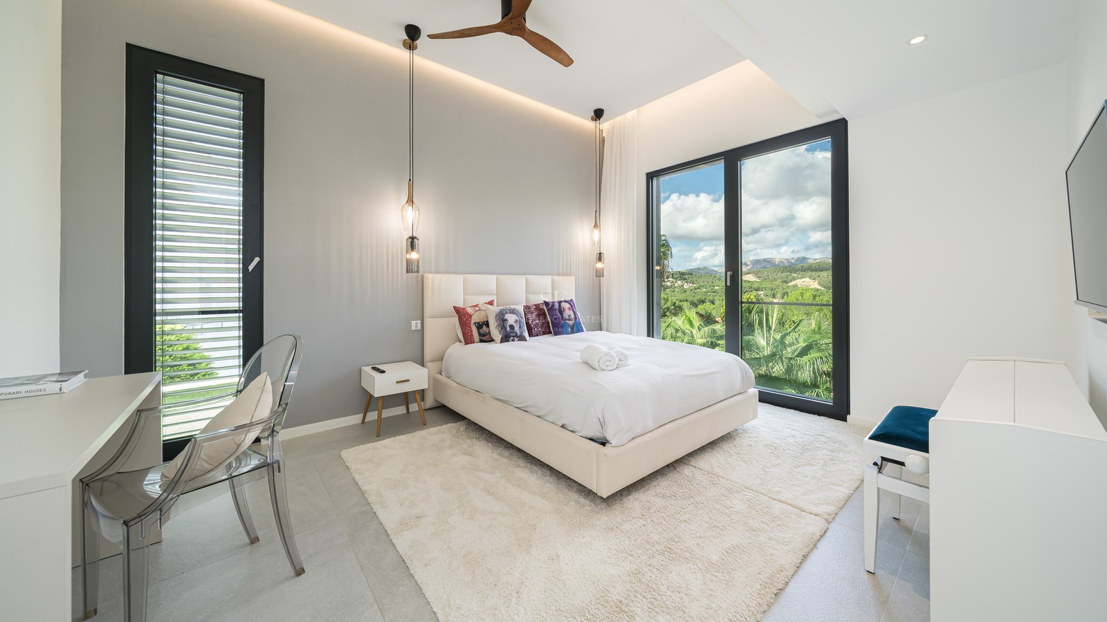 Chambre moderne avec grand lit, baies vitrées donnant sur les montagnes, chaise transparente et éclairage design.