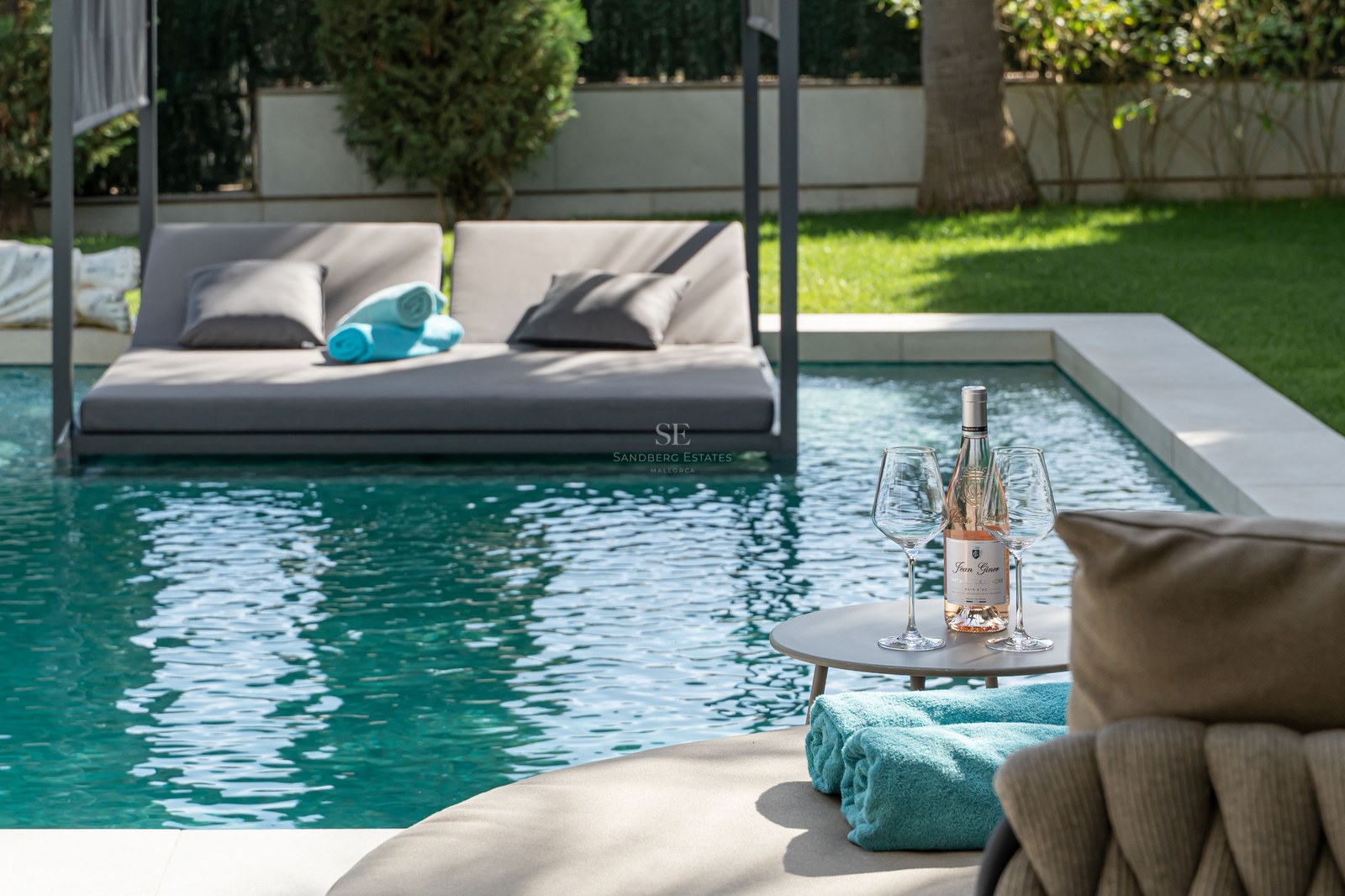 Piscine de luxe avec un lit de repos flottant gris, une table avec du vin rosé et des serviettes turquoise.
