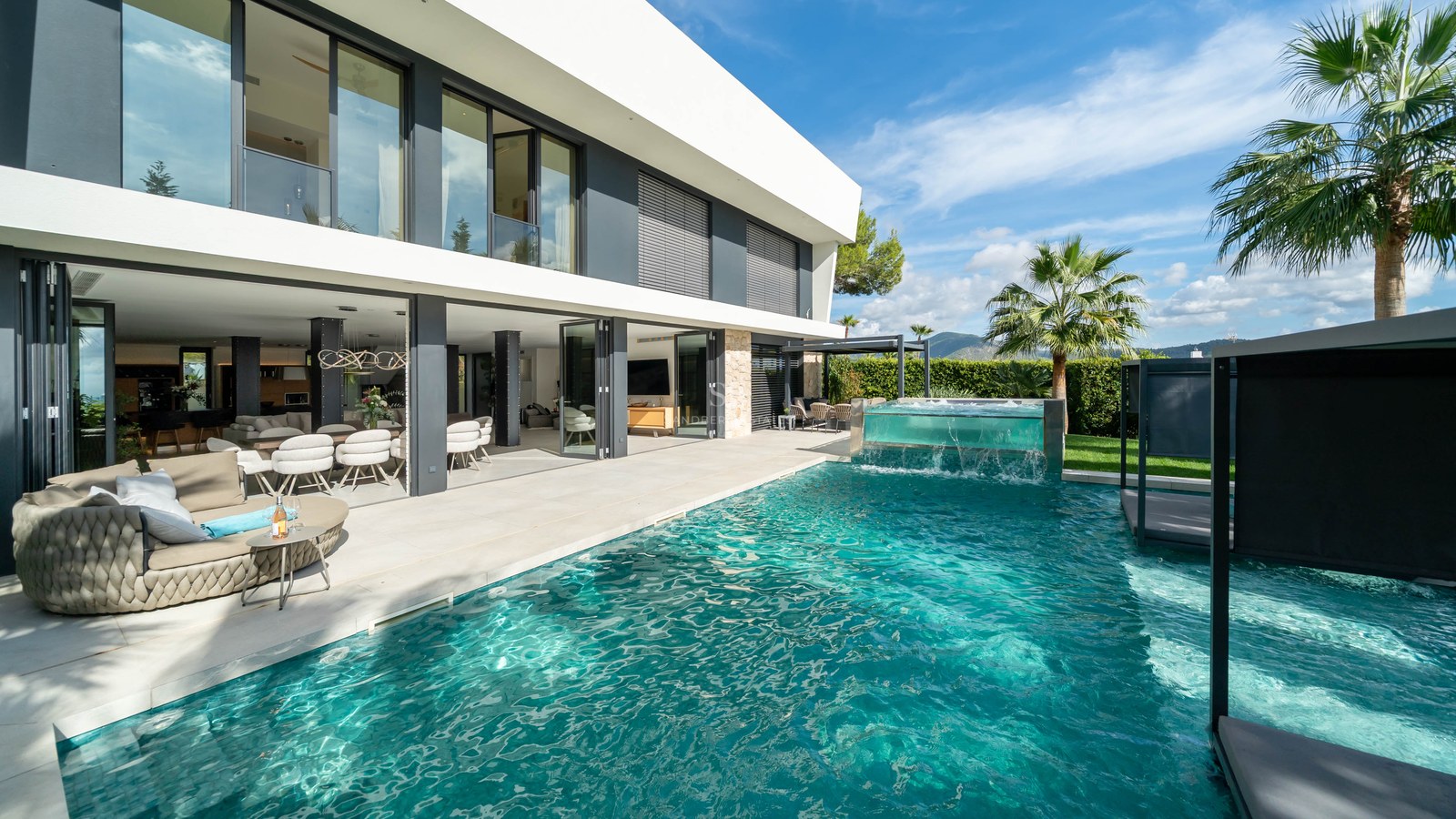 Villa de luxe avec piscine turquoise, jacuzzi aux parois en verre et terrasse ouverte sous un ciel bleu.