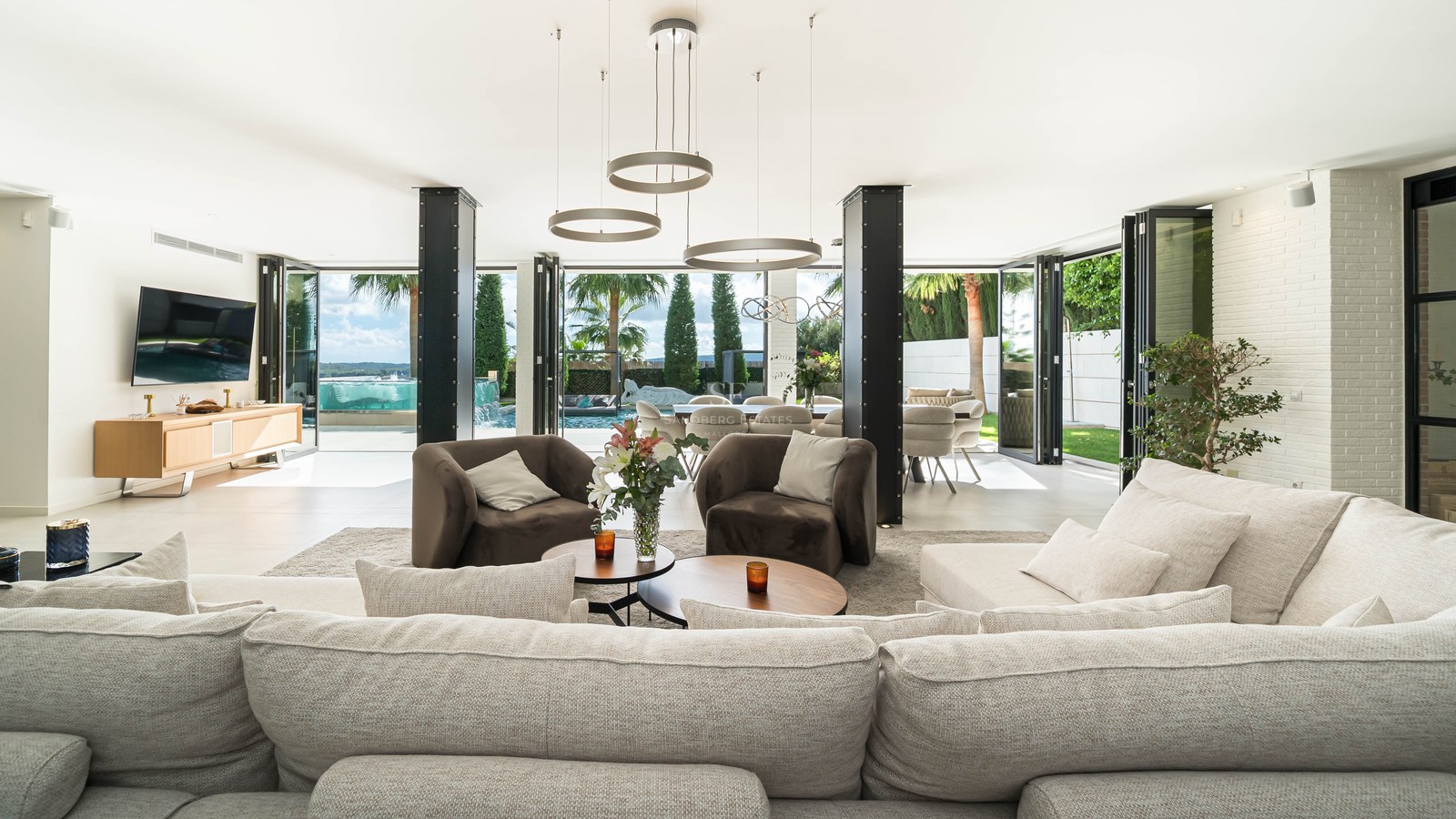Salon moderne avec canapé d'angle crème, piliers en acier et baies vitrées accordéon ouvrant sur la piscine.