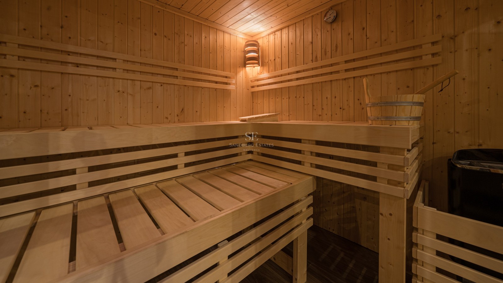 Vue intérieure d'un sauna en bois avec bancs à plusieurs niveaux, éclairage d'angle chaleureux et seau en bois.
