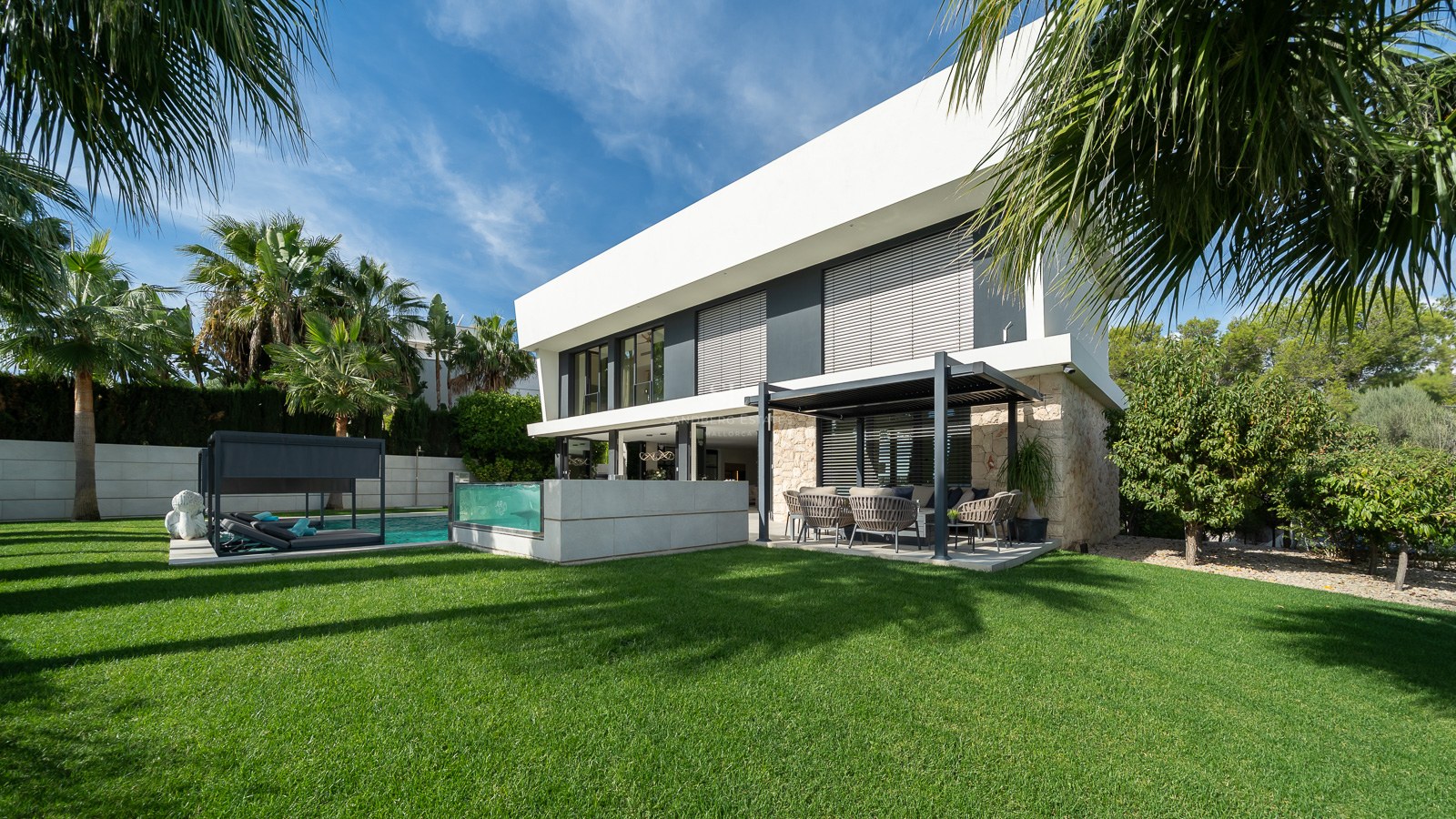 Villa moderne de deux étages avec pierre, piscine à paroi de verre et terrasse couverte sur une pelouse verdoyante.