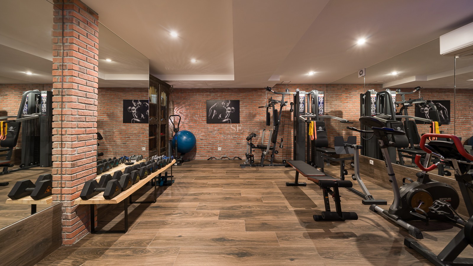 Salle de sport avec murs en briques, parquet, grands miroirs et équipements de fitness professionnels.