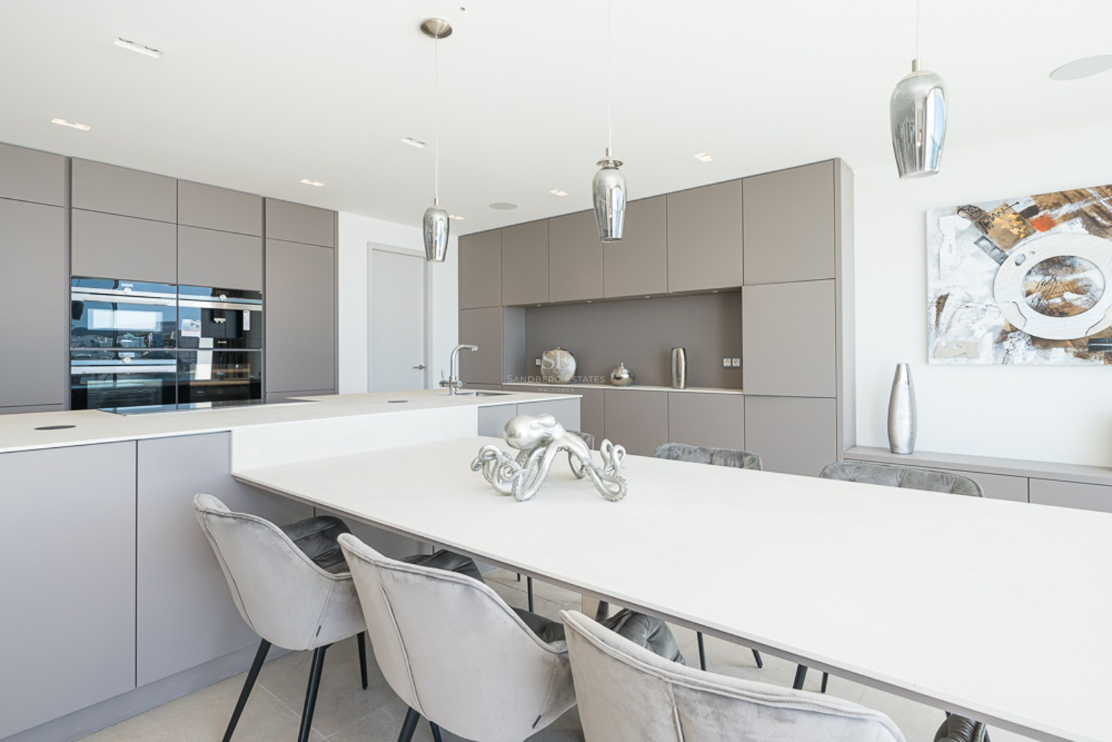 Cocina contemporánea con armarios color topo, una gran isla blanca y sillas de comedor de terciopelo gris.