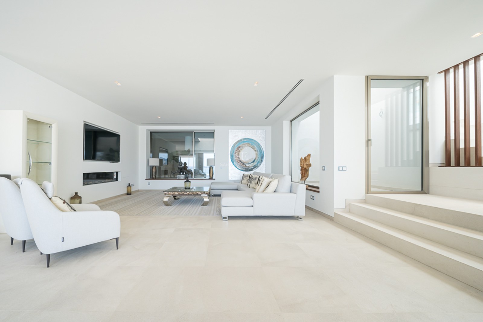 Salón minimalista luminoso con sofá blanco, suelos de piedra, chimenea lineal y arte moderno.