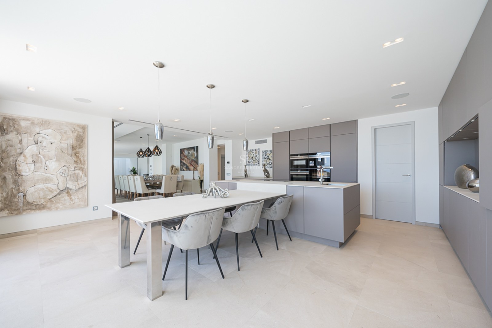 Cocina moderna con armarios grises, isla blanca con mesa de comedor y sillas de terciopelo gris.