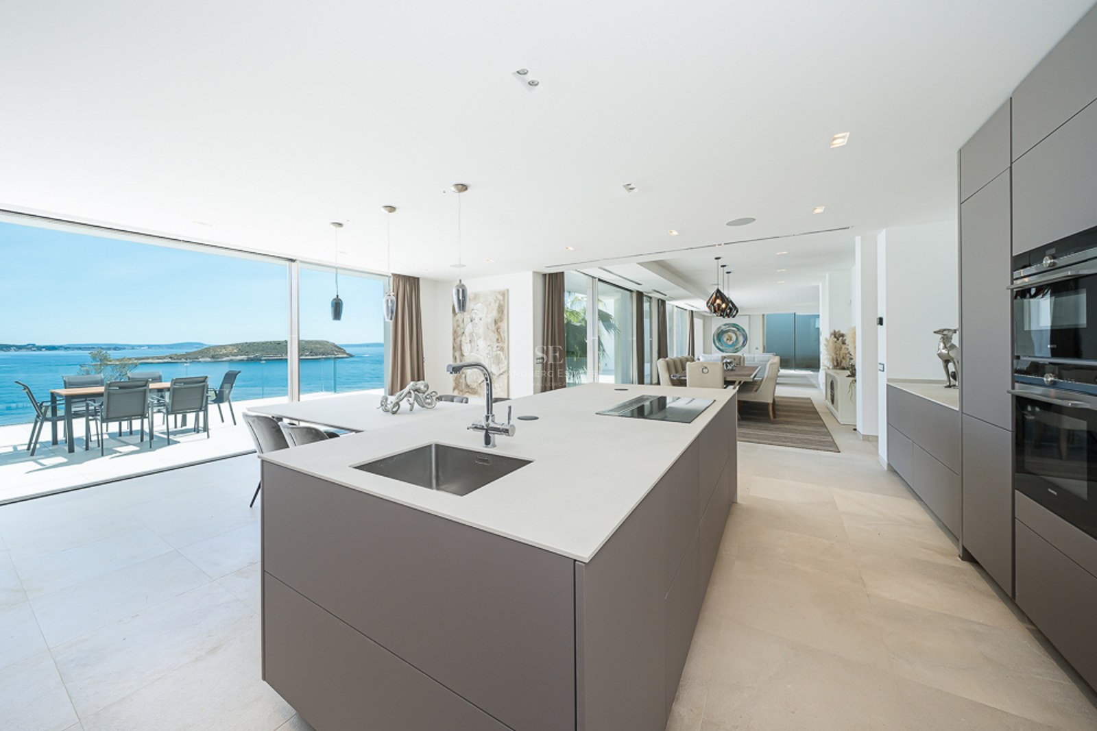 Isla de cocina minimalista frente a una terraza con vistas al océano y una isla a lo lejos.