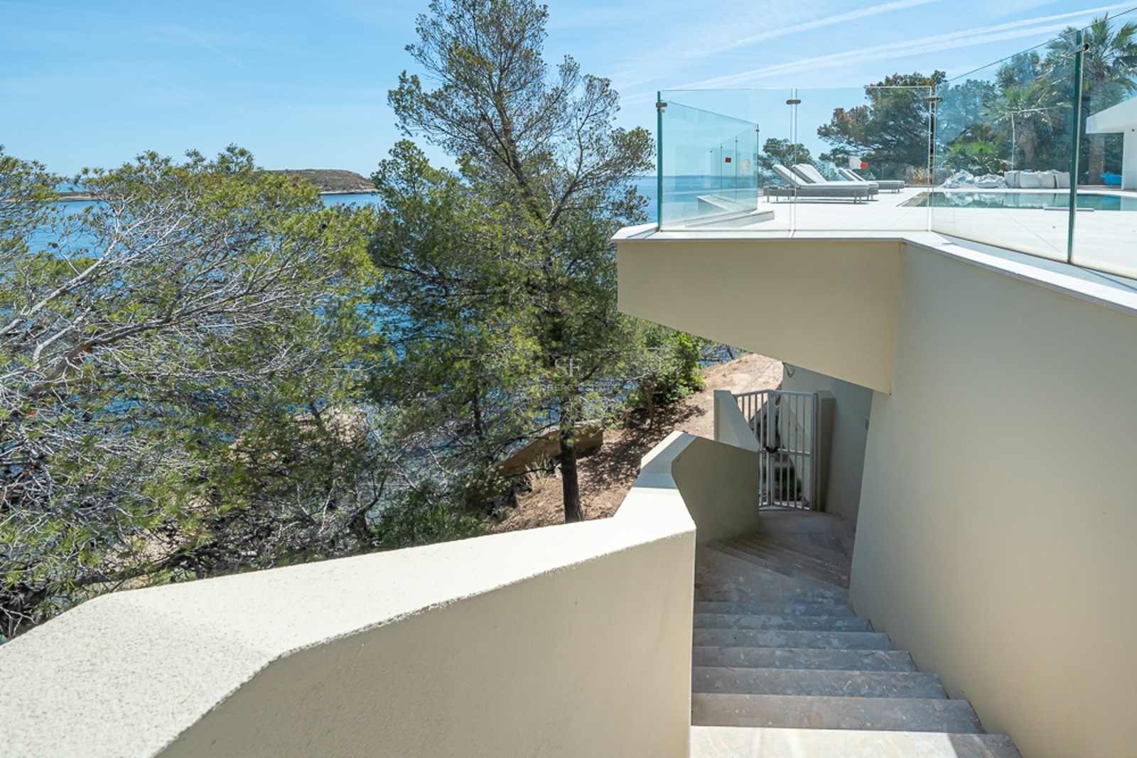 Terraza de lujo con barandillas de cristal y escaleras de piedra con vistas al mar Mediterráneo y pinos.