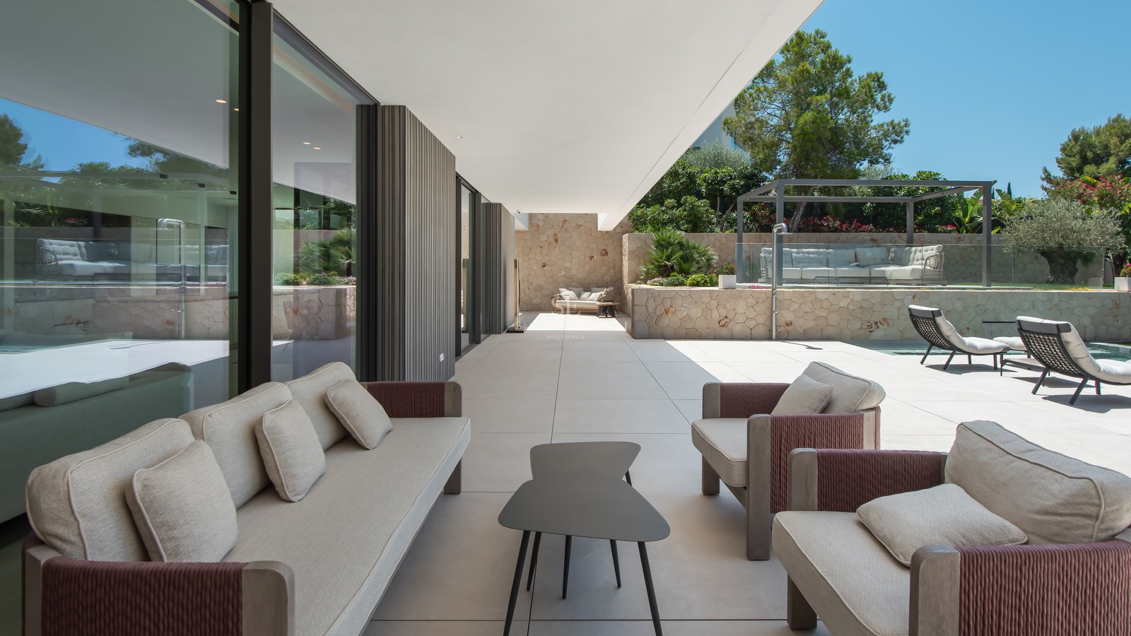 Vaste terrasse moderne avec mobilier de salon haut de gamme, murs en pierre et baies vitrées coulissantes.