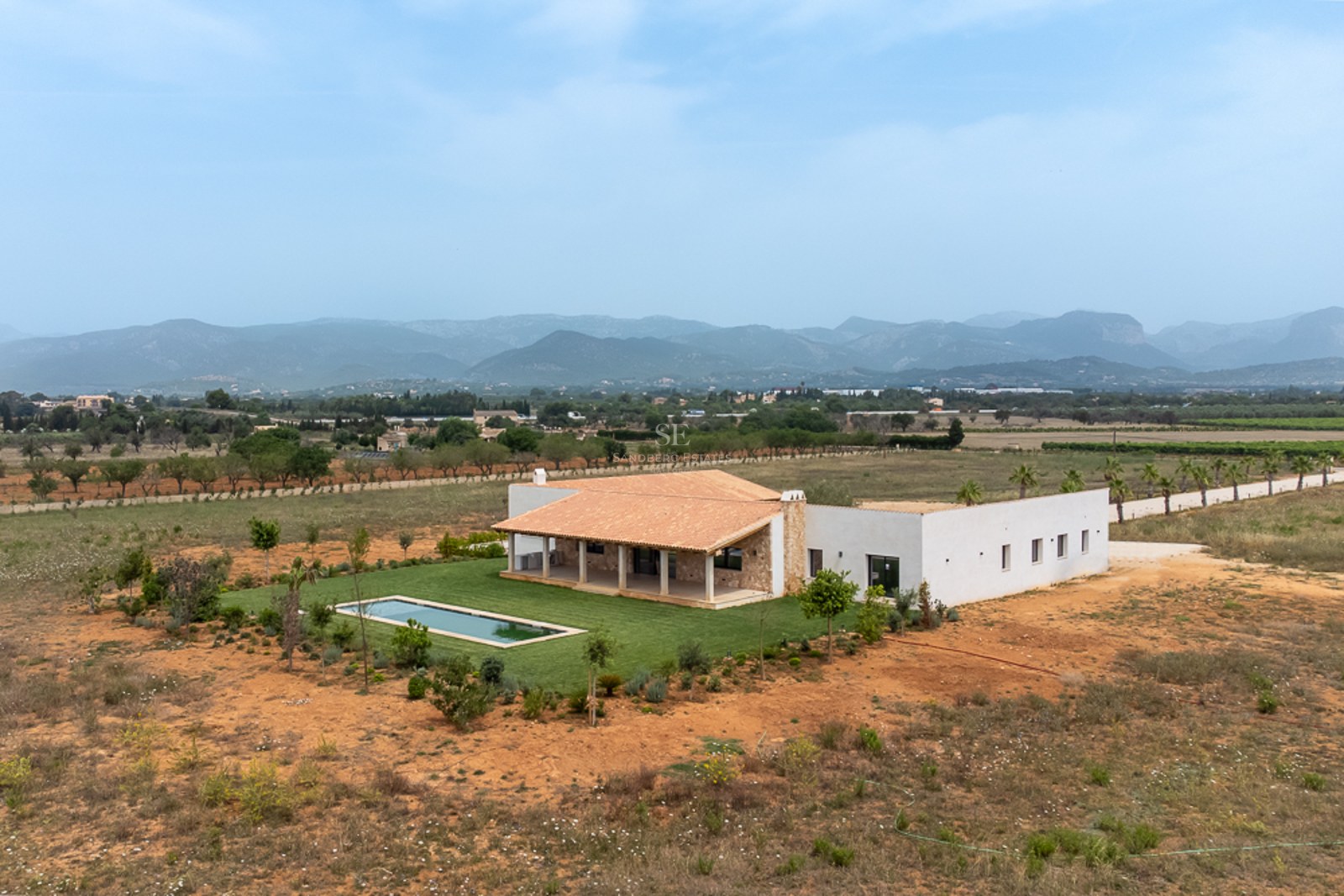Luftaufnahme einer weißen Villa mit Pool, Terrakottadach und großem Grundstück vor Bergkulisse.