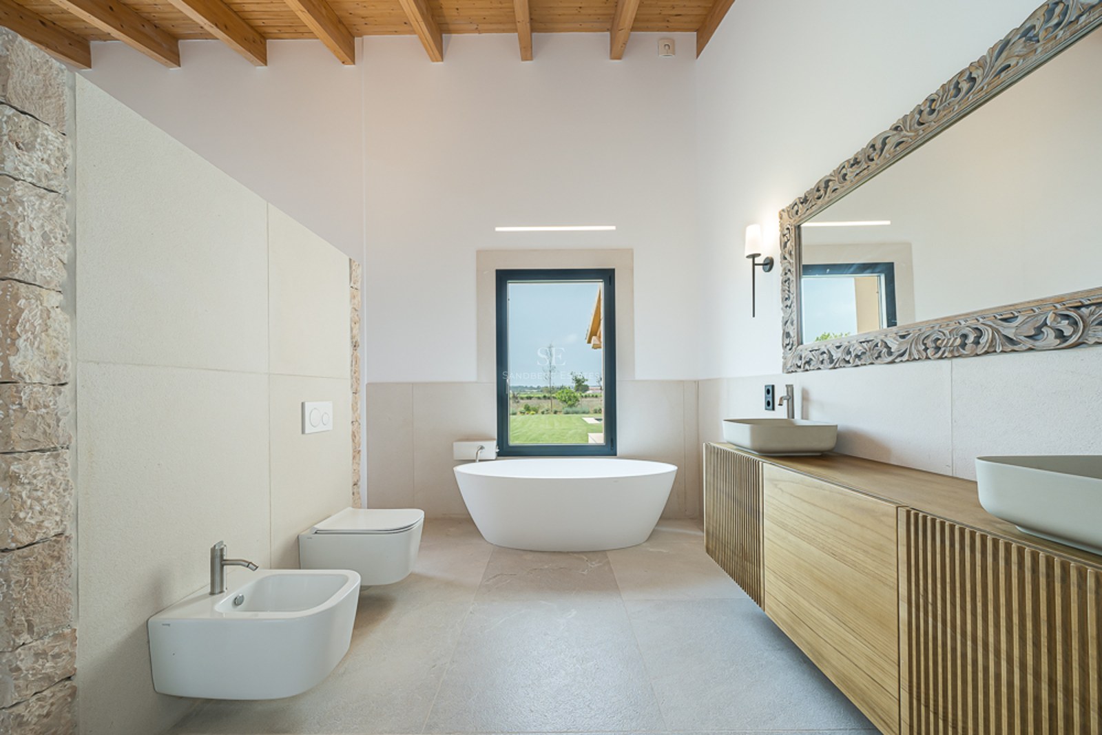 Luxuriöses Badezimmer mit freistehender Badewanne, Holzbalkendecke, Natursteinwand und Doppelwaschtisch.