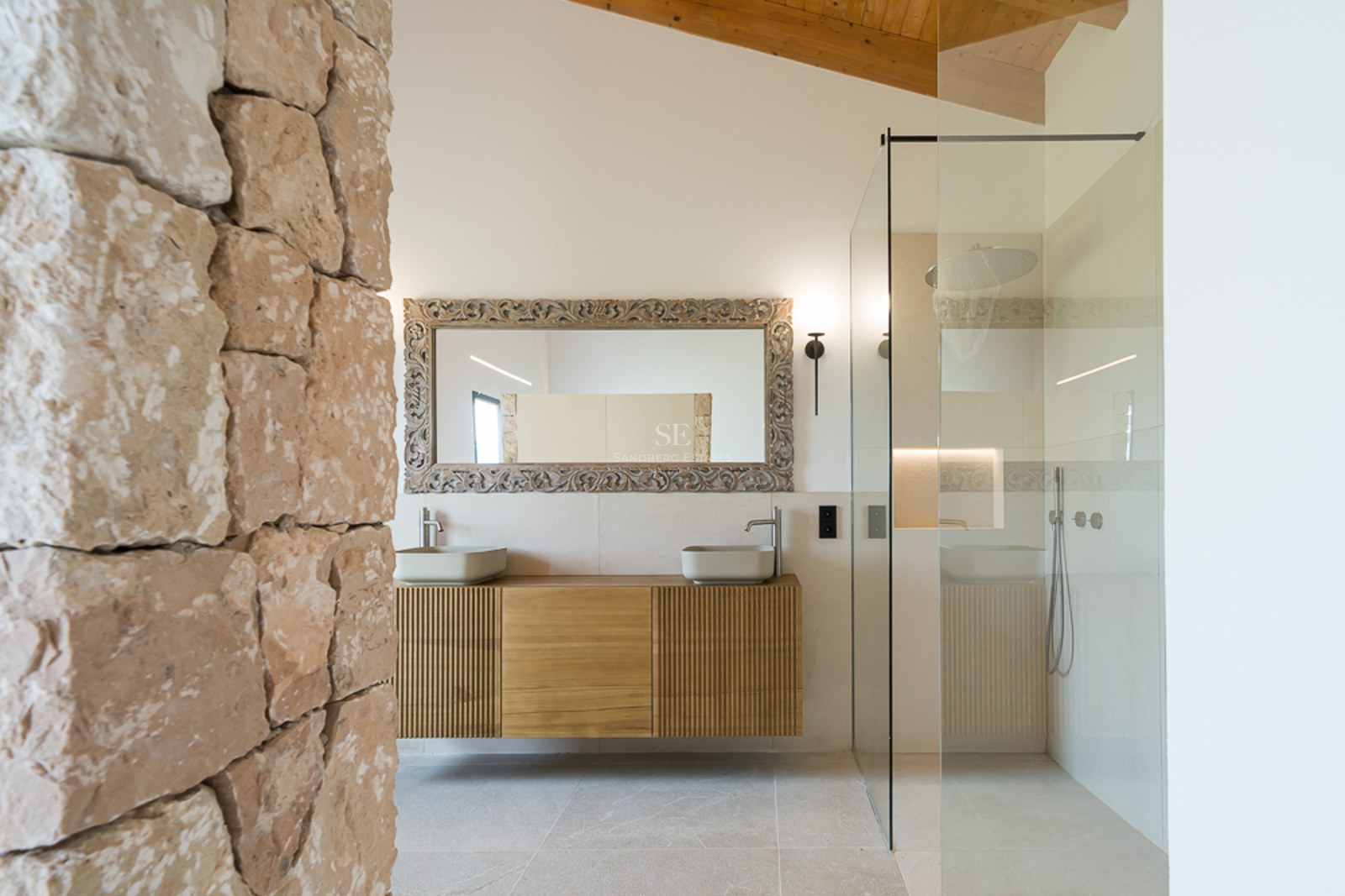 Modernes Badezimmer mit rustikaler Steinwand, Holzbalkendecke, Glasdusche und schwebendem Doppelwaschtisch.