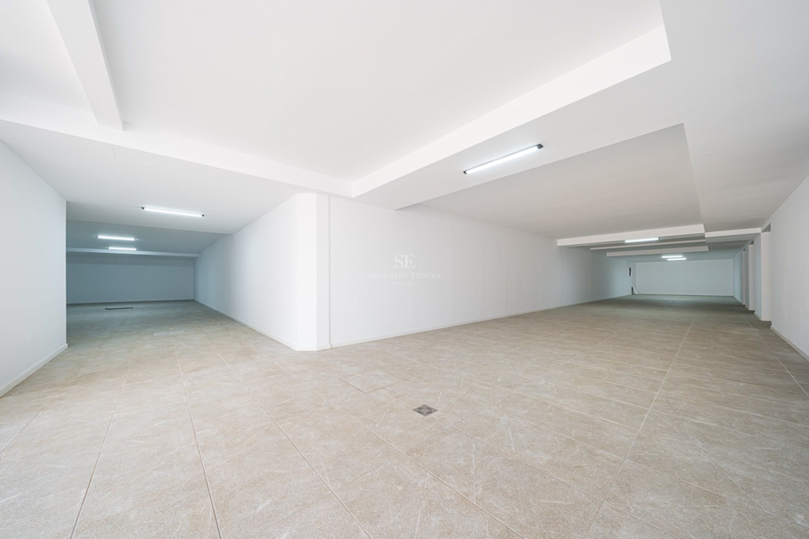 Große leere Tiefgarage mit weißen Wänden, beigefarbenen Fliesen und moderner LED-Beleuchtung.