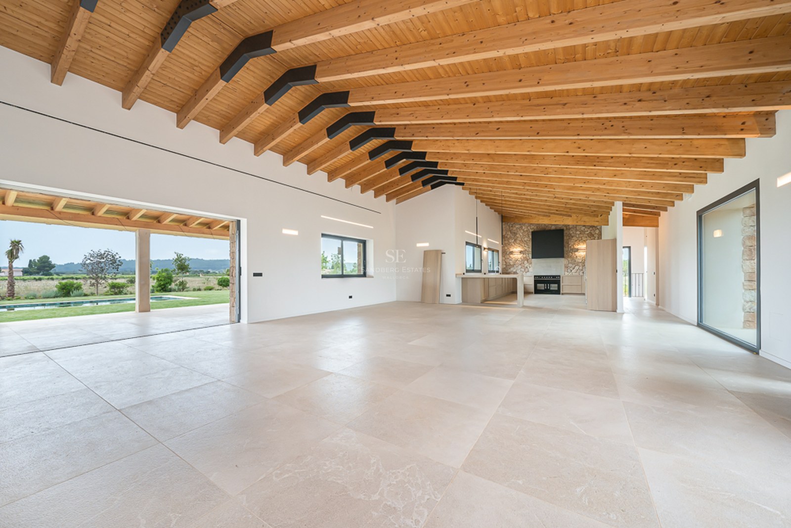 Großes modernes Wohnzimmer mit Holzbalkendecke, Steinfußboden und Glasschiebetüren zum Pool und Garten.