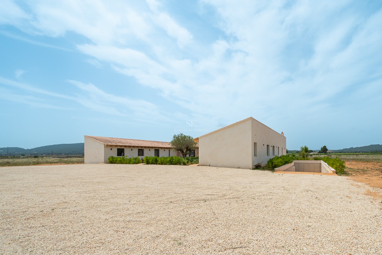 L-förmige cremefarbene minimalistische Villa mit Terrakottadach und Kiesauffahrt unter strahlend blauem Himmel.