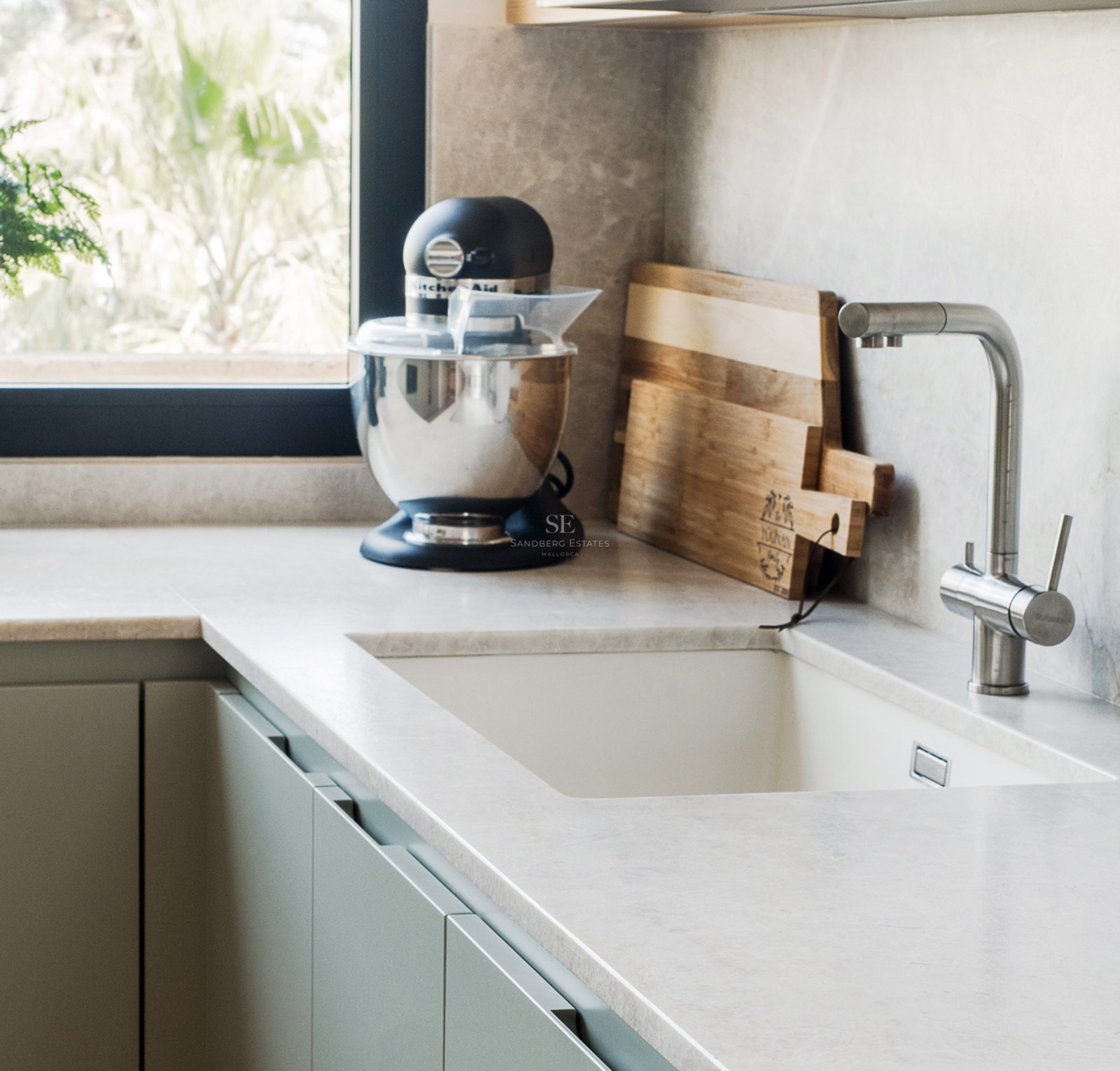 Primer plano de un fregadero de cocina con grifo de acero, encimera de piedra, batidora y tablas de madera.