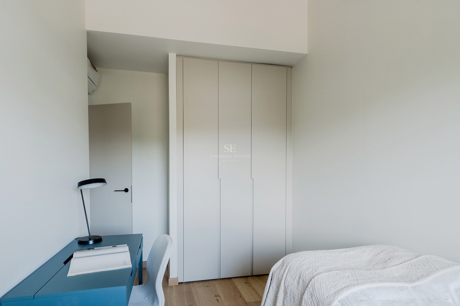 Dormitorio moderno con armario empotrado blanco, escritorio azul, lámpara negra y suelo de madera clara.