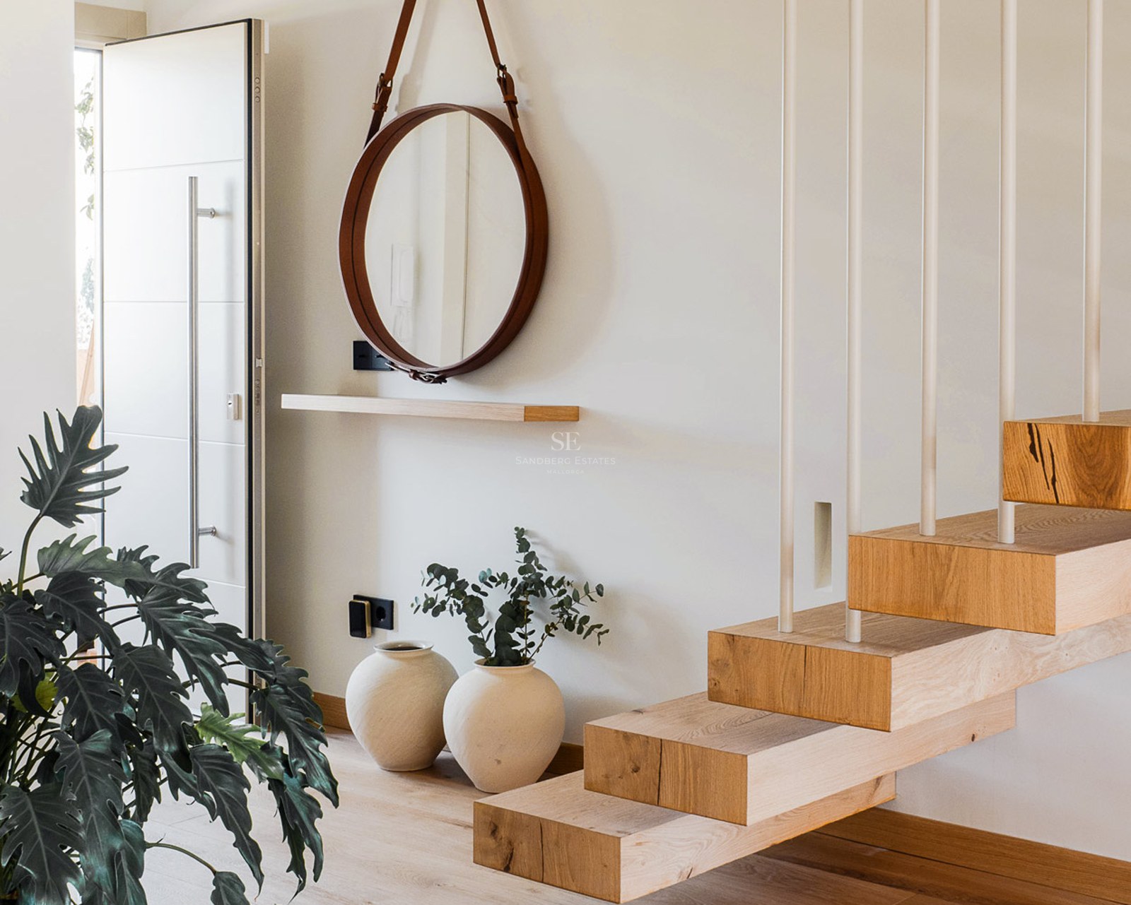Entrada con escalones de madera flotantes, espejo circular con correa de cuero y decoración minimalista.