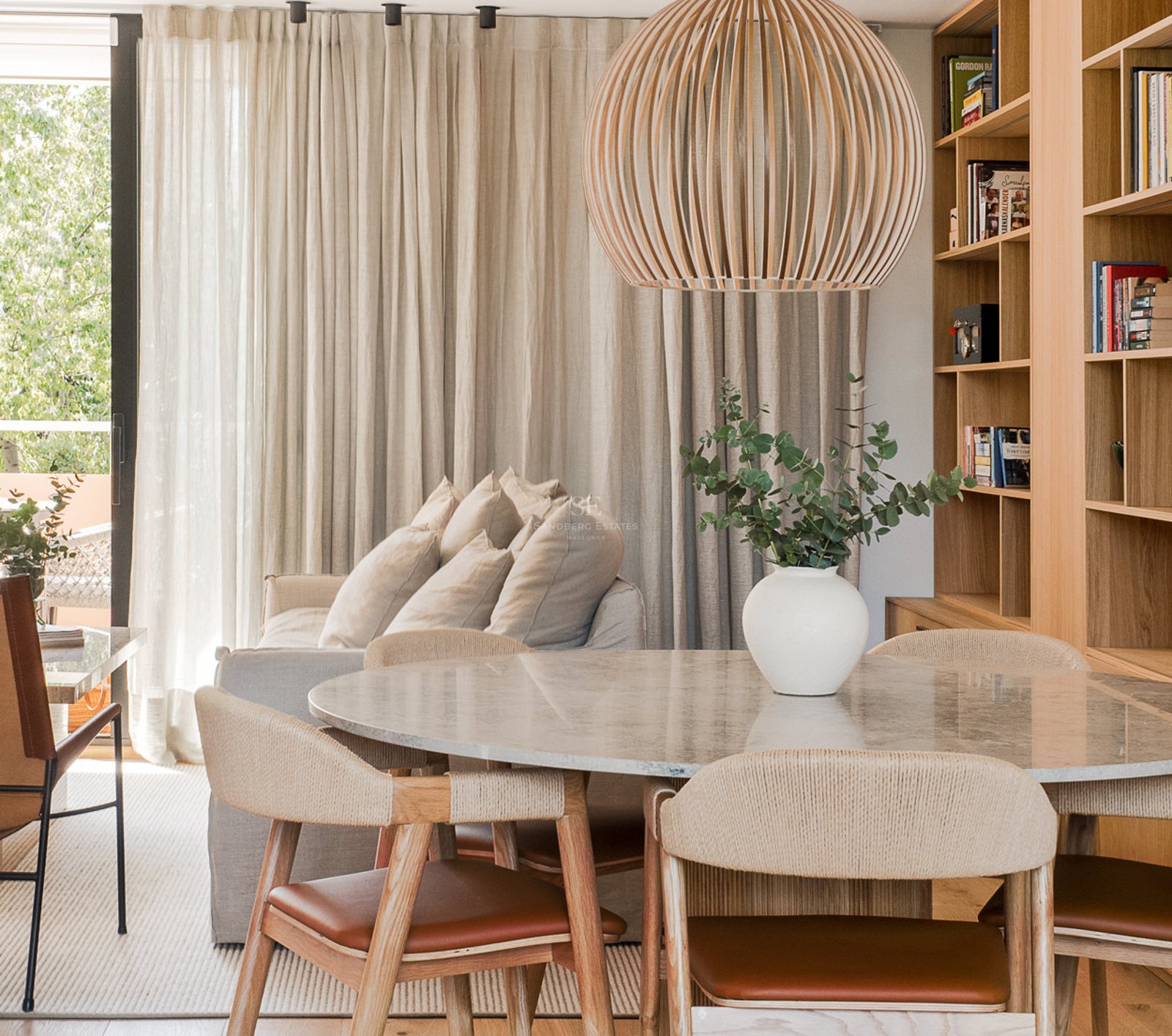 Comedor luminoso con mesa de mármol, sillas de madera y cuero, y una gran lámpara colgante de listones de madera.