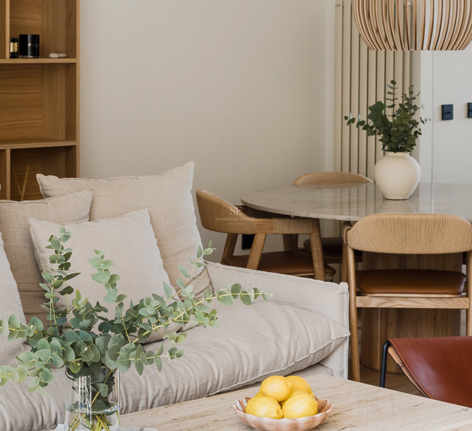 Sala de estar moderna con sofá beige, mesa de comedor de piedra y decoración minimalista con eucalipto.