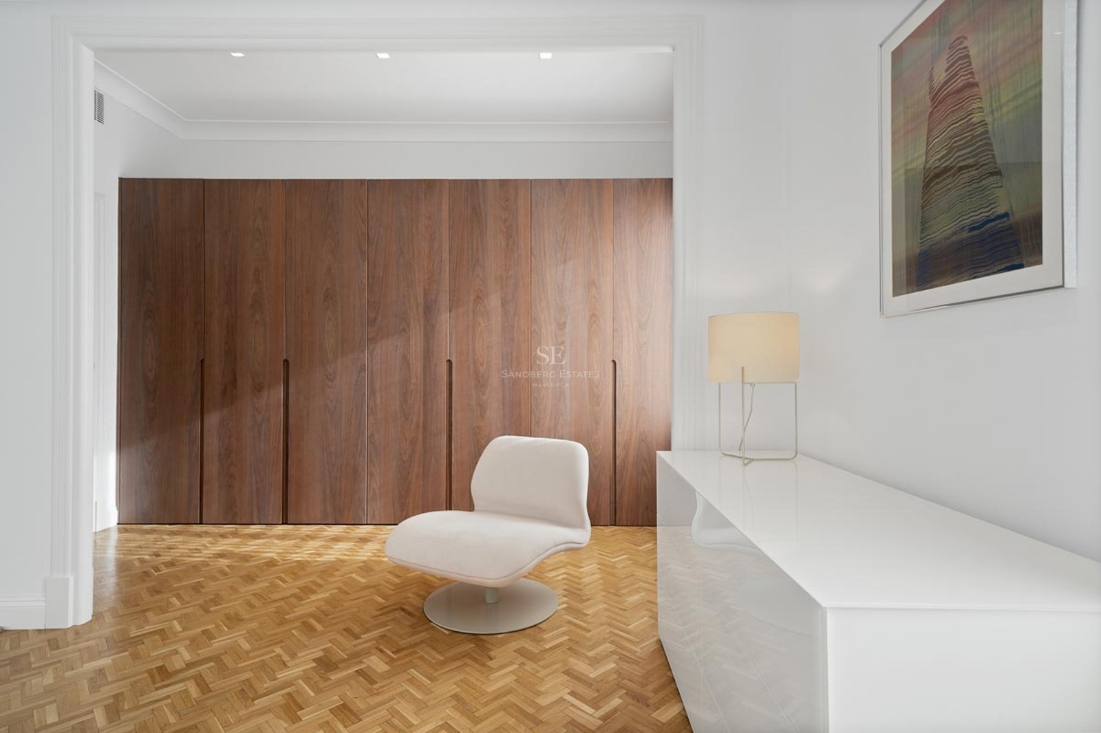 Espace dressing minimaliste avec placards en bois, parquet à chevrons et fauteuil design blanc.