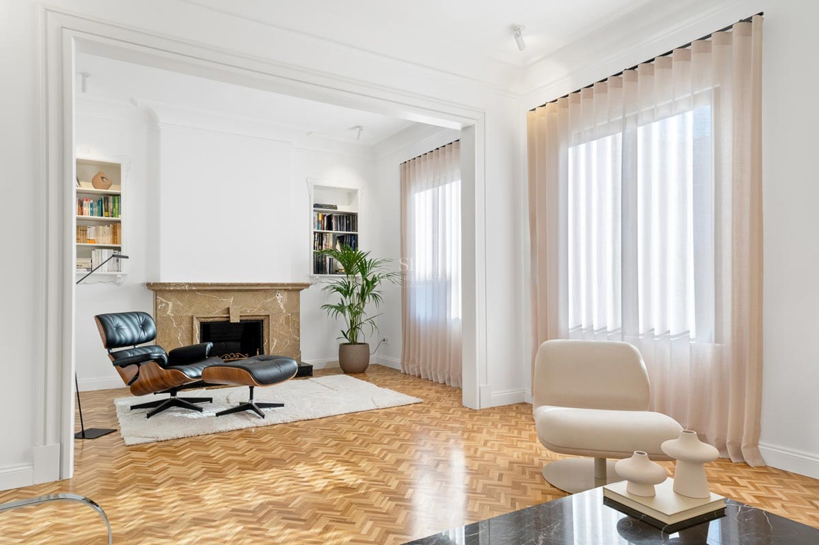 Salon lumineux avec parquet en chevrons, cheminée en marbre et fauteuil Eames.