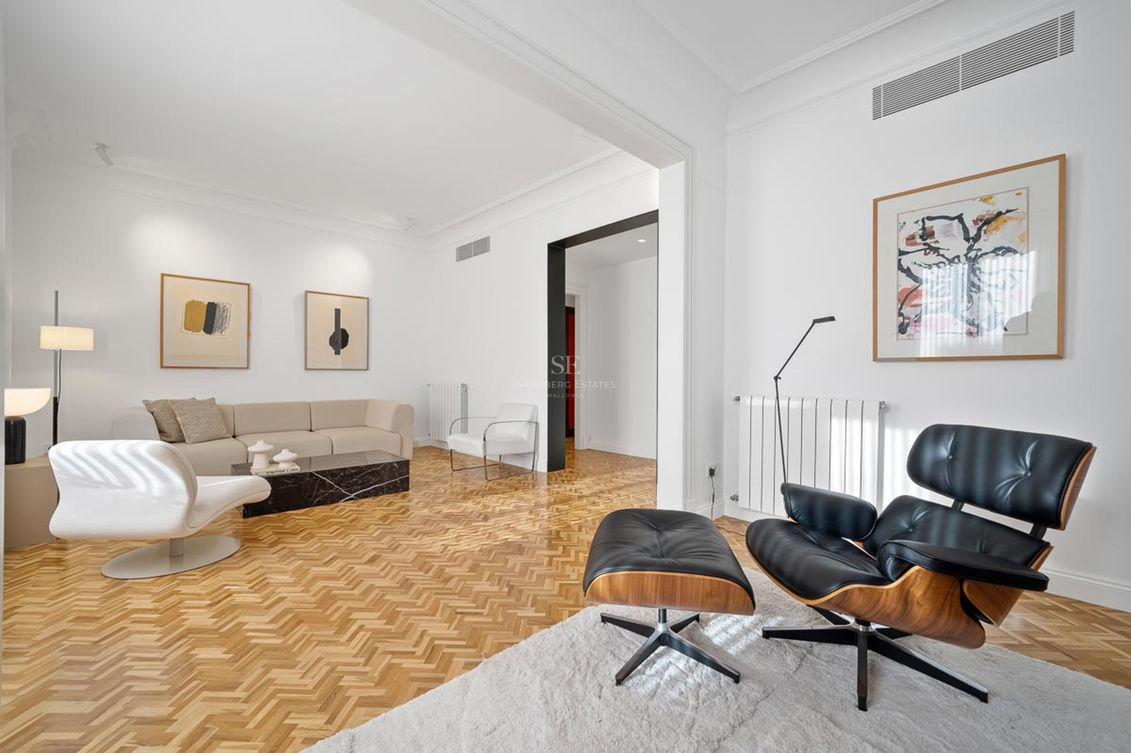 Salon lumineux avec canapé beige, fauteuil Eames noir, table en marbre noir et parquet en chevrons.