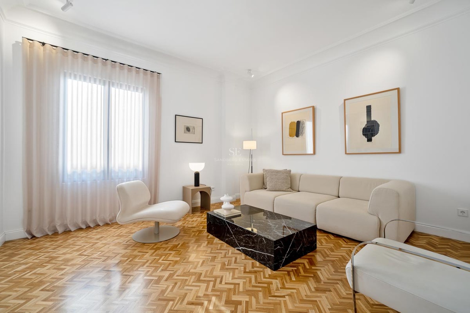 Salon lumineux avec murs blancs, parquet en chevrons, canapé beige et table basse en marbre noir.