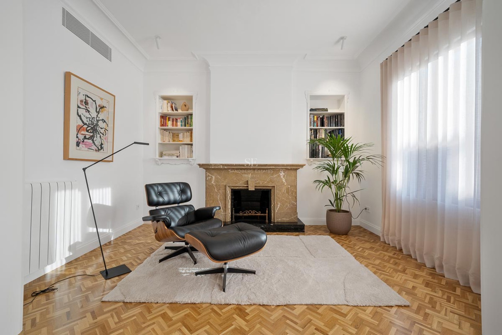 Salon moderne avec fauteuil Eames en cuir, cheminée en marbre, parquet et étagères intégrées.