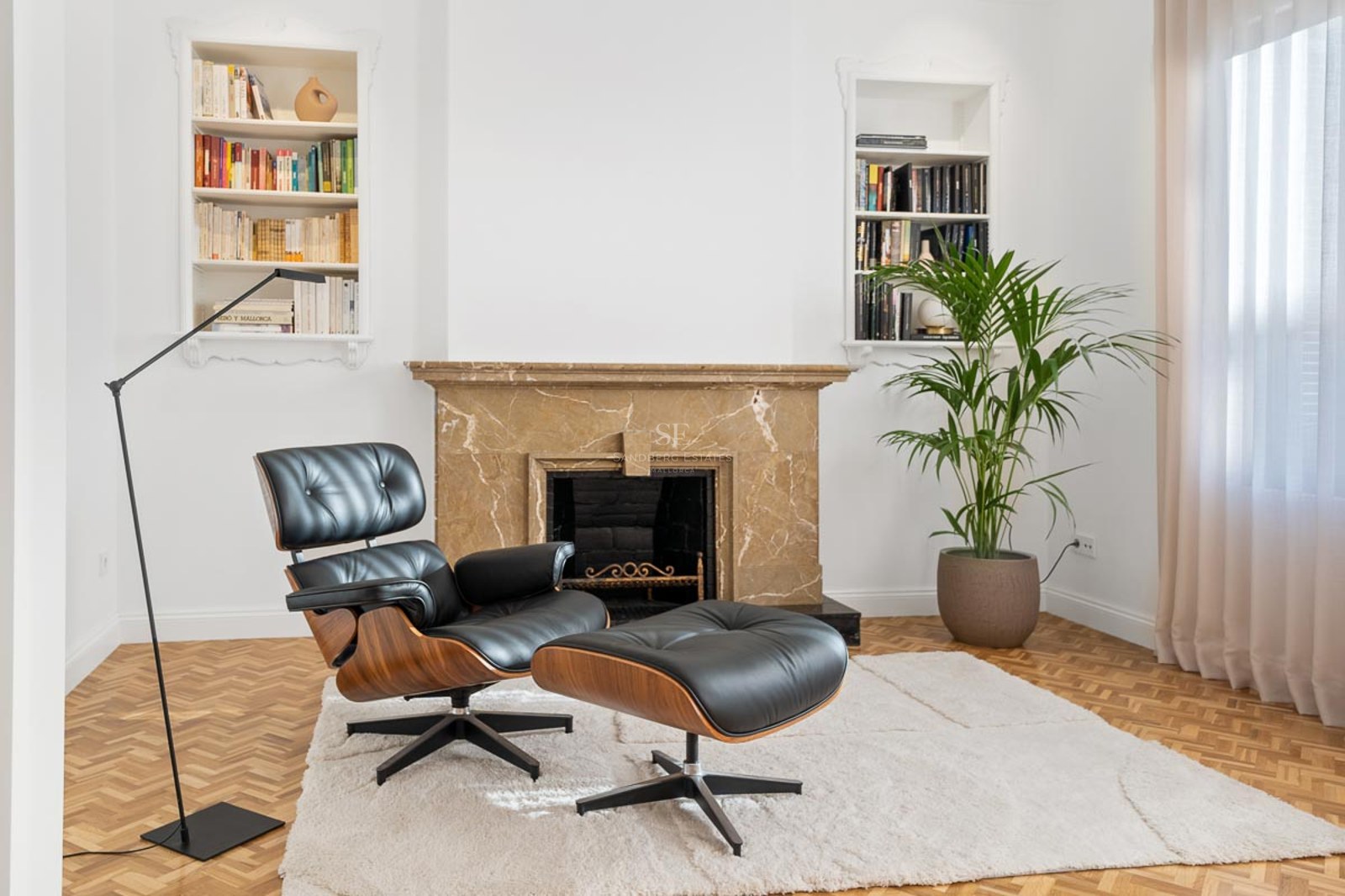 Fauteuil en cuir noir et repose-pieds devant une cheminée en marbre et des bibliothèques encastrées.