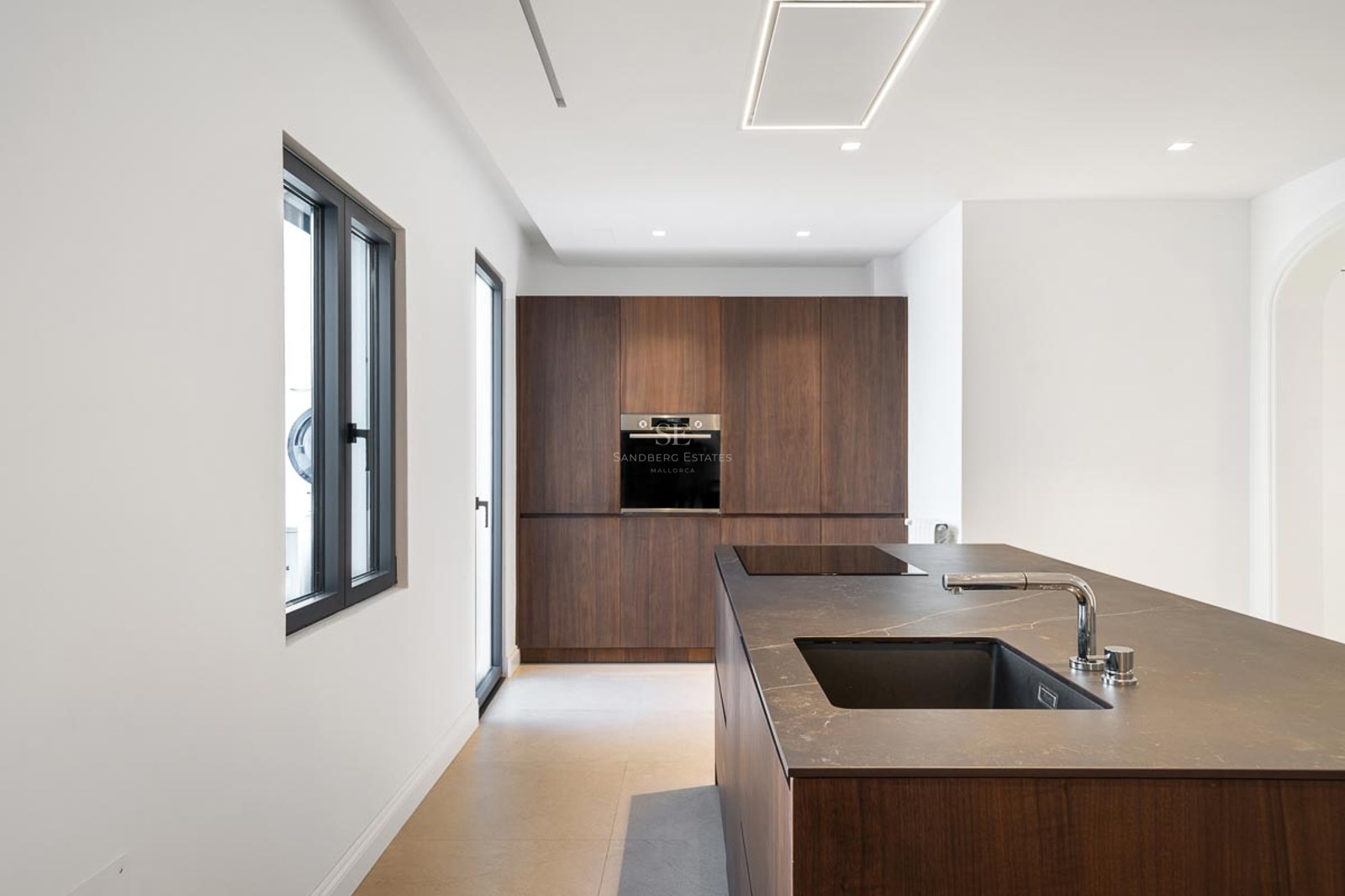 Cuisine moderne avec îlot en bois sombre, plan de travail noir, évier intégré et armoires encastrées.