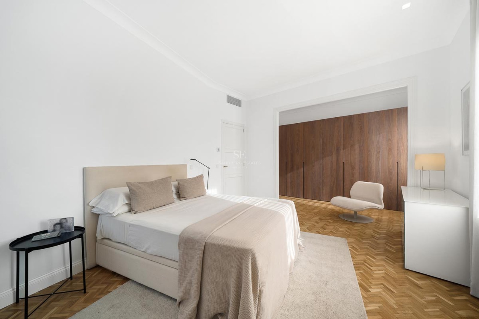 Chambre de maître minimaliste et lumineuse avec un grand lit, un sol en chevrons et des armoires en bois du sol au plafond.