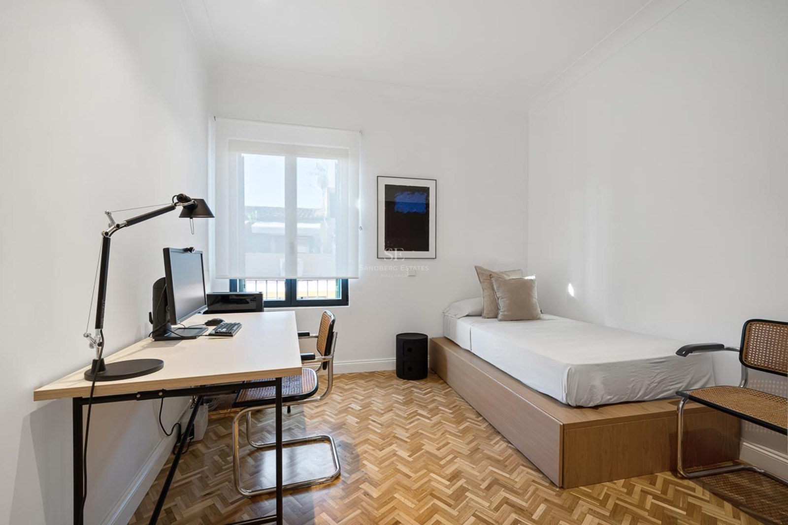 Chambre lumineuse avec lit simple, parquet en chevrons et bureau avec ordinateur.