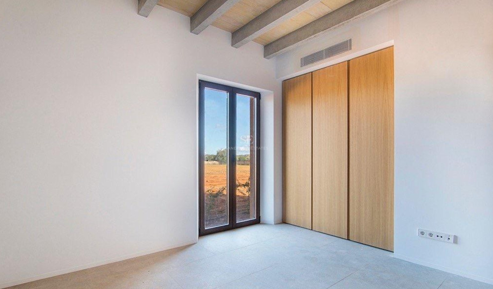 Bright bedroom with wooden ceiling beams, built-in oak wardrobes, and a window overlooking a rural landscape.