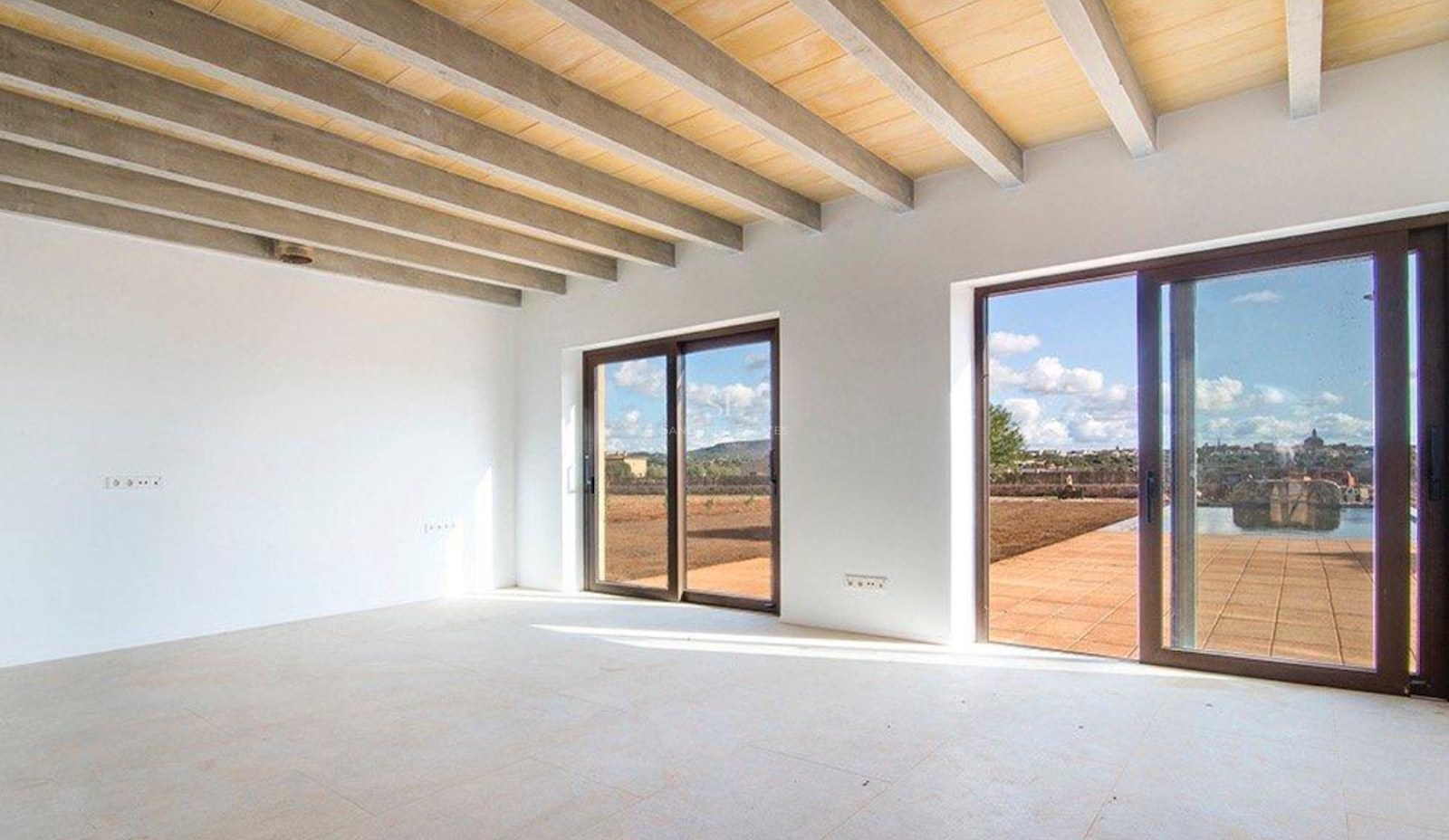 Spacious empty room with exposed concrete and wood ceiling beams, white walls, and sliding glass doors to a terrace.